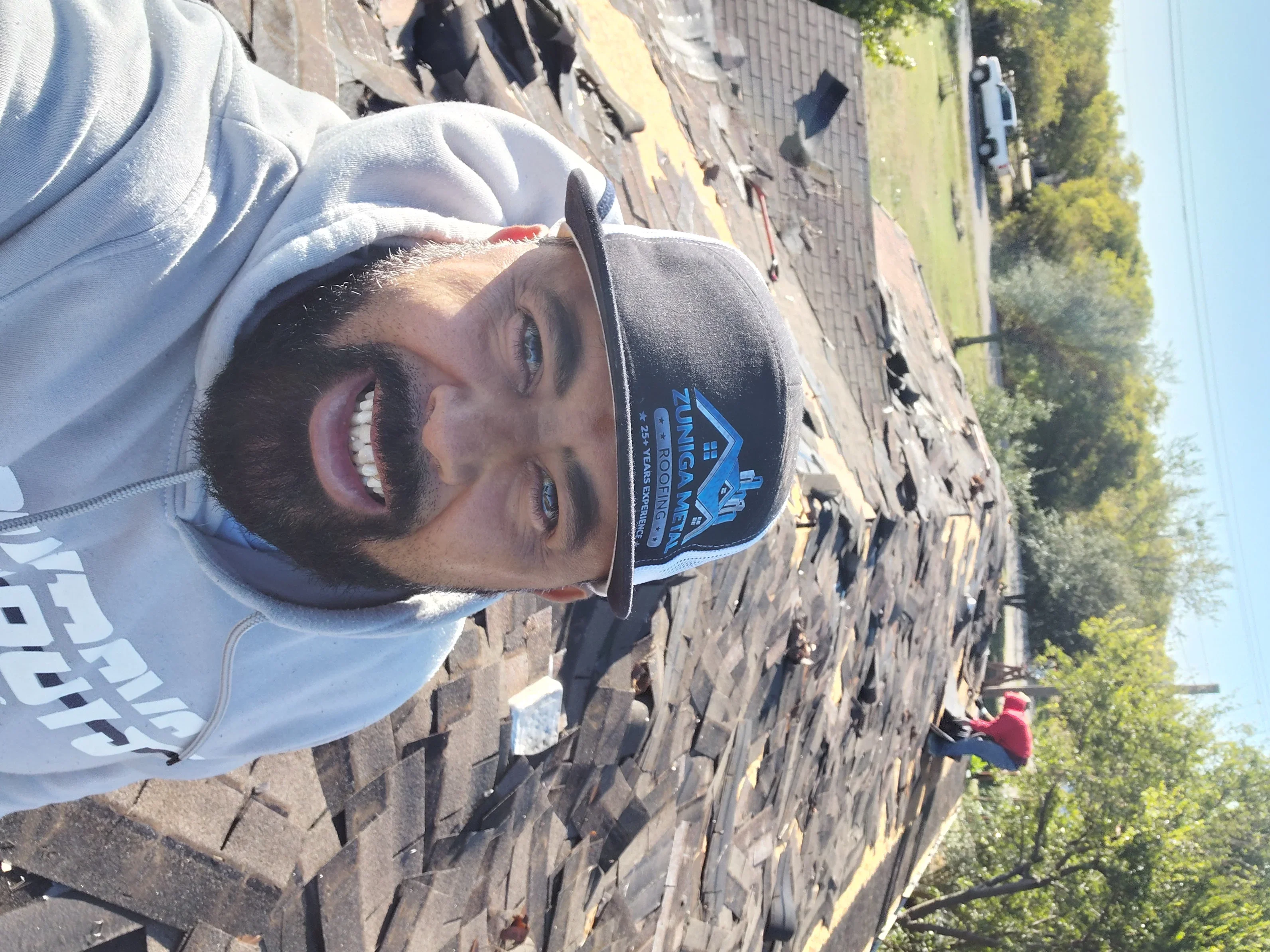Worker installing dark asphalt shingles on residential roof with proper overlap and fastening