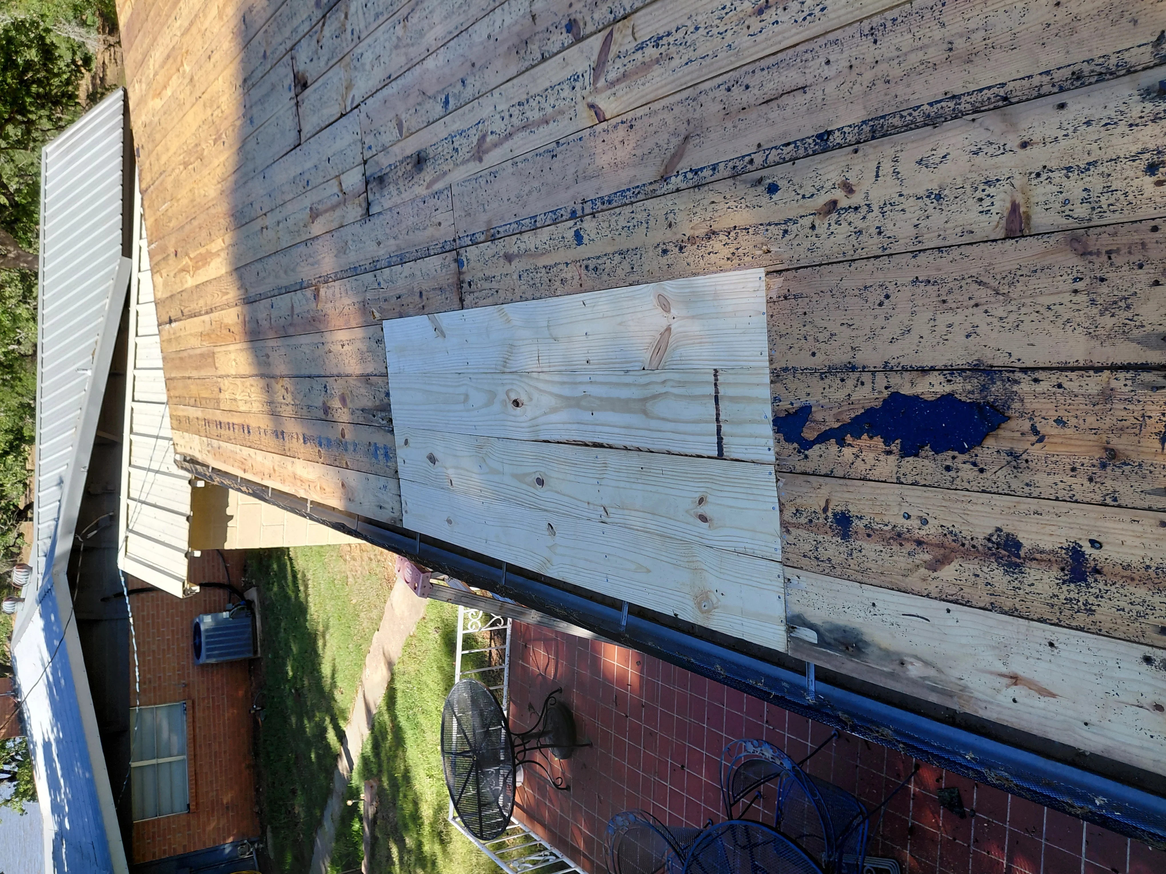 Wood shingle roof repair with new light-colored shingles replacing weathered, dark-stained sections