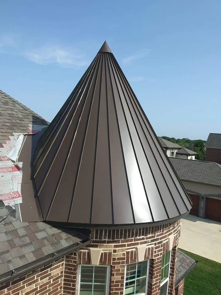 Dark standing seam metal roof on conical turret with vertical panel lines and brick base