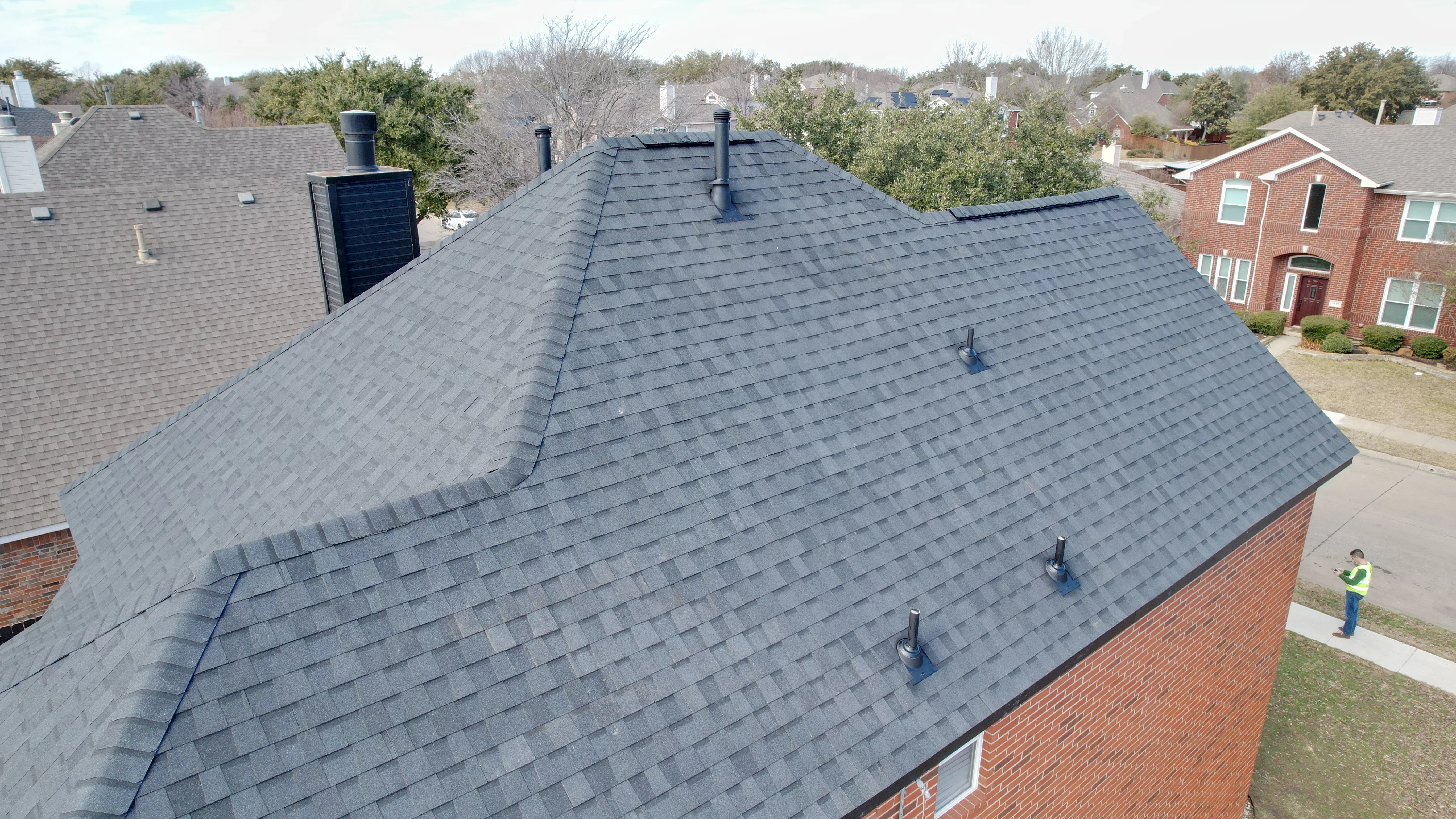Charcoal gray architectural shingle roof with multiple vent penetrations and flashing on brick home