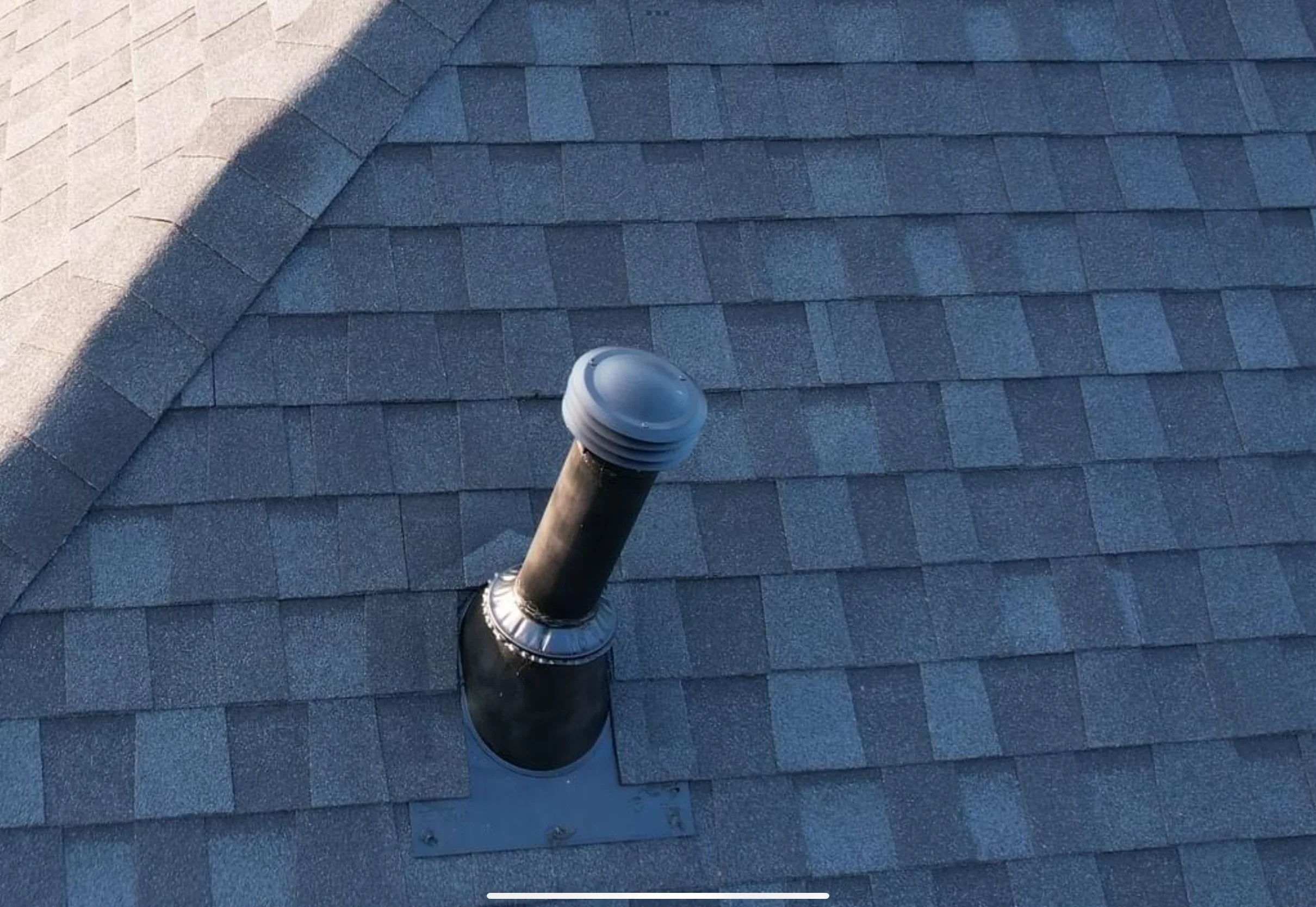 Black metal roof vent with flashing installed on blue-gray asphalt shingles