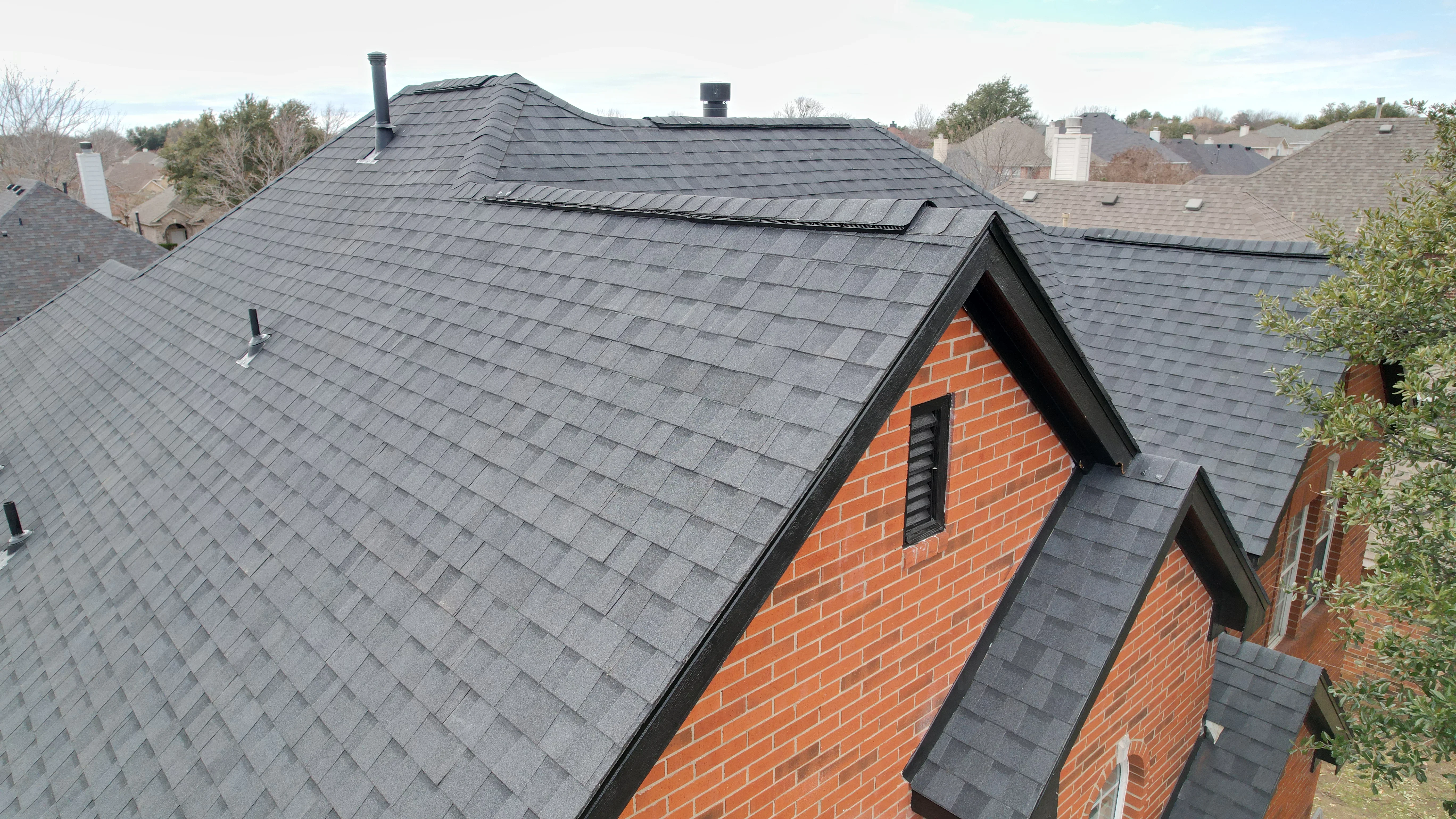Charcoal metal roof with standing seam panels on brick home with dormers and multiple roof planes