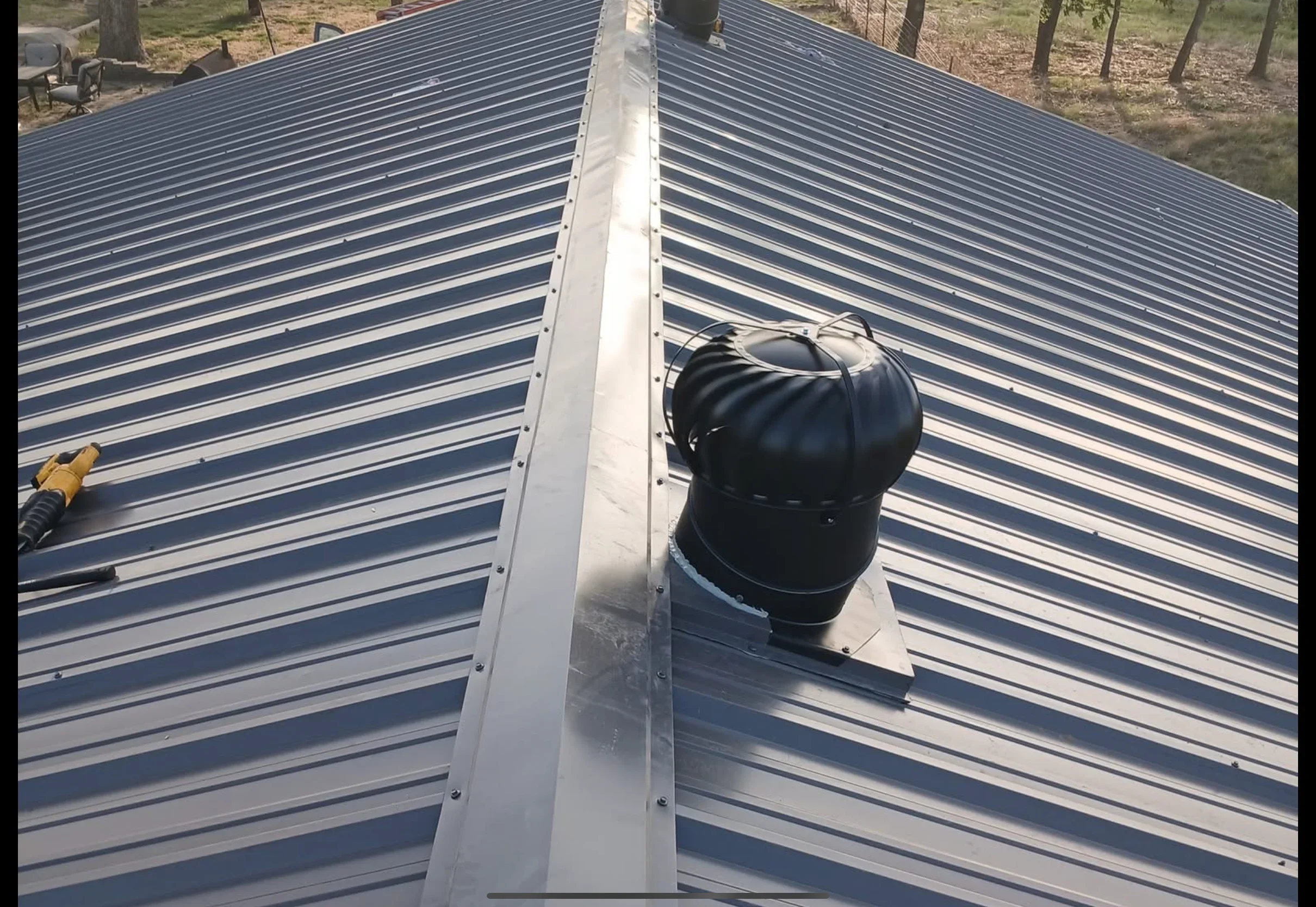 Standing seam metal roof with charcoal panels, white ridge cap, and black roof vent installation