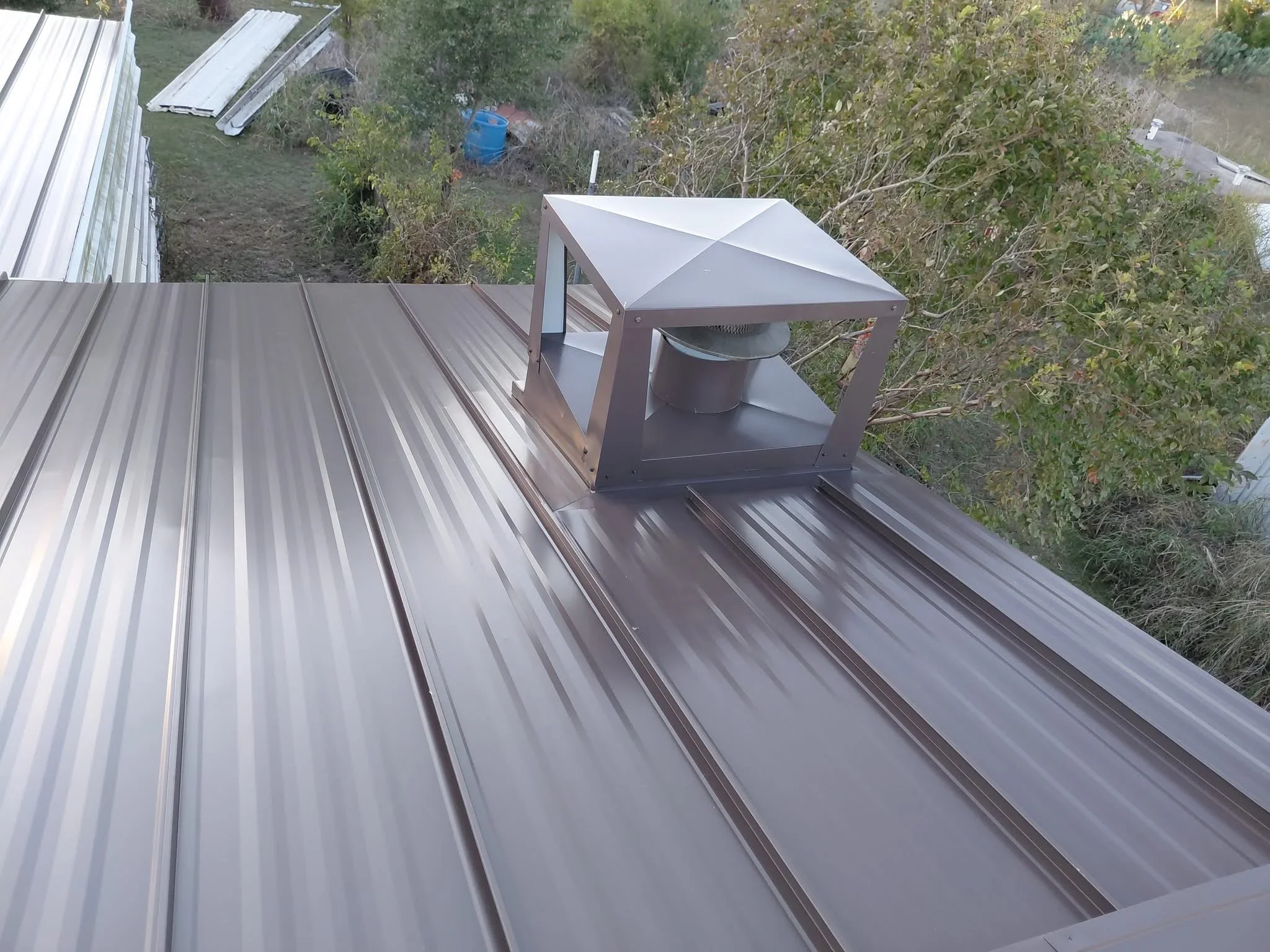 Standing seam metal roof with brown chimney flashing and cap installation
