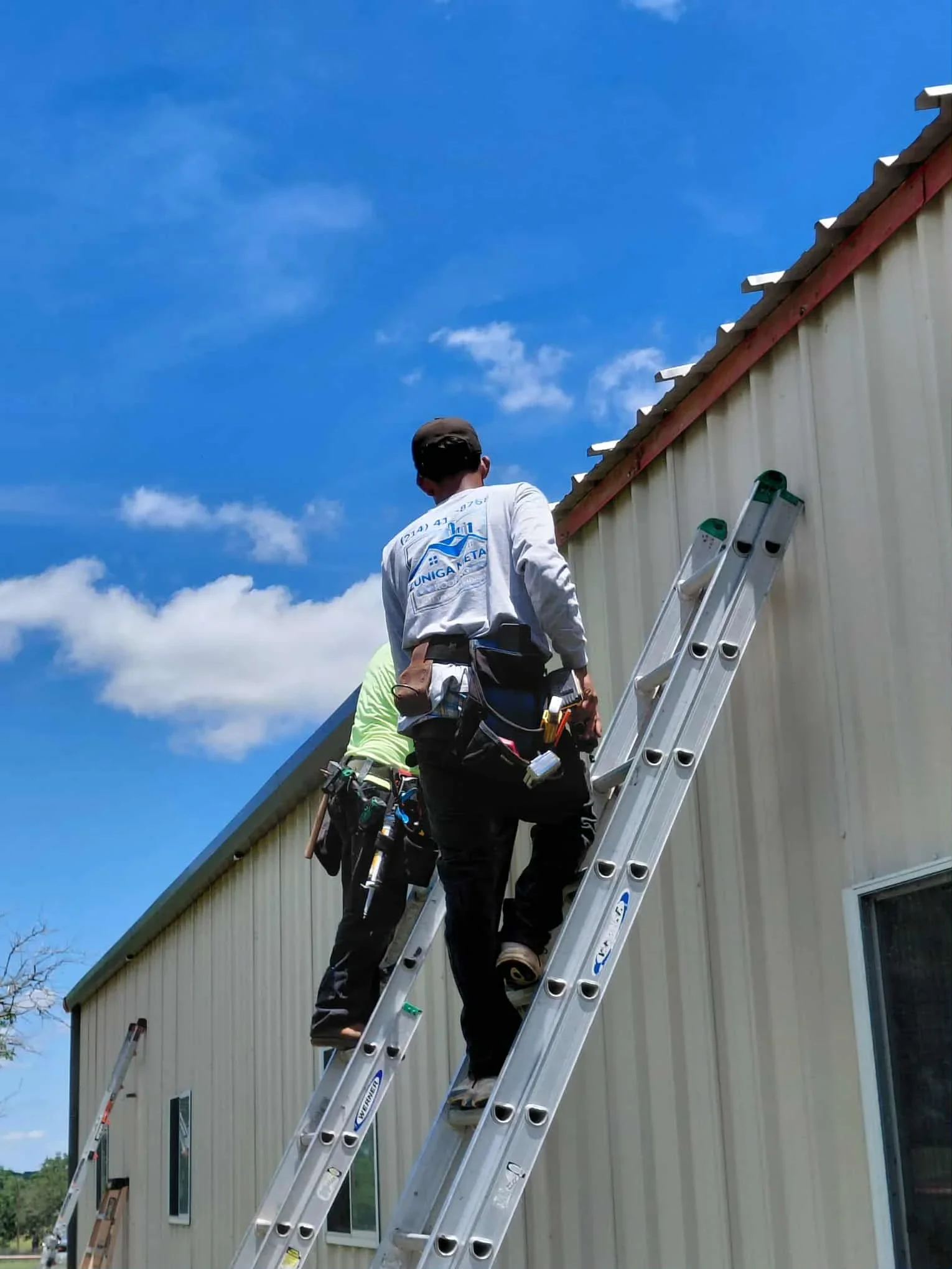 Worker installing standing seam metal roofing panels on commercial building with ladder access