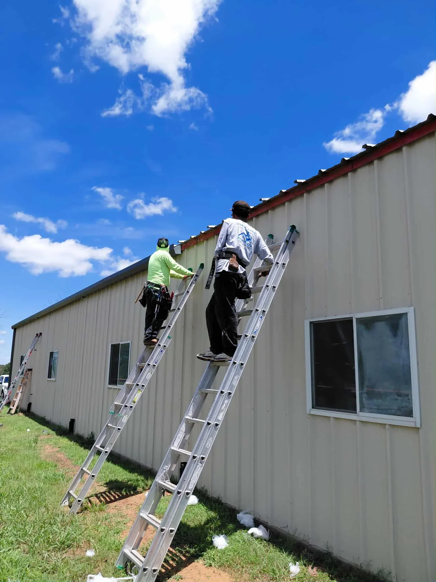 Two workers installing standing seam metal roof on commercial building with corrugated metal siding