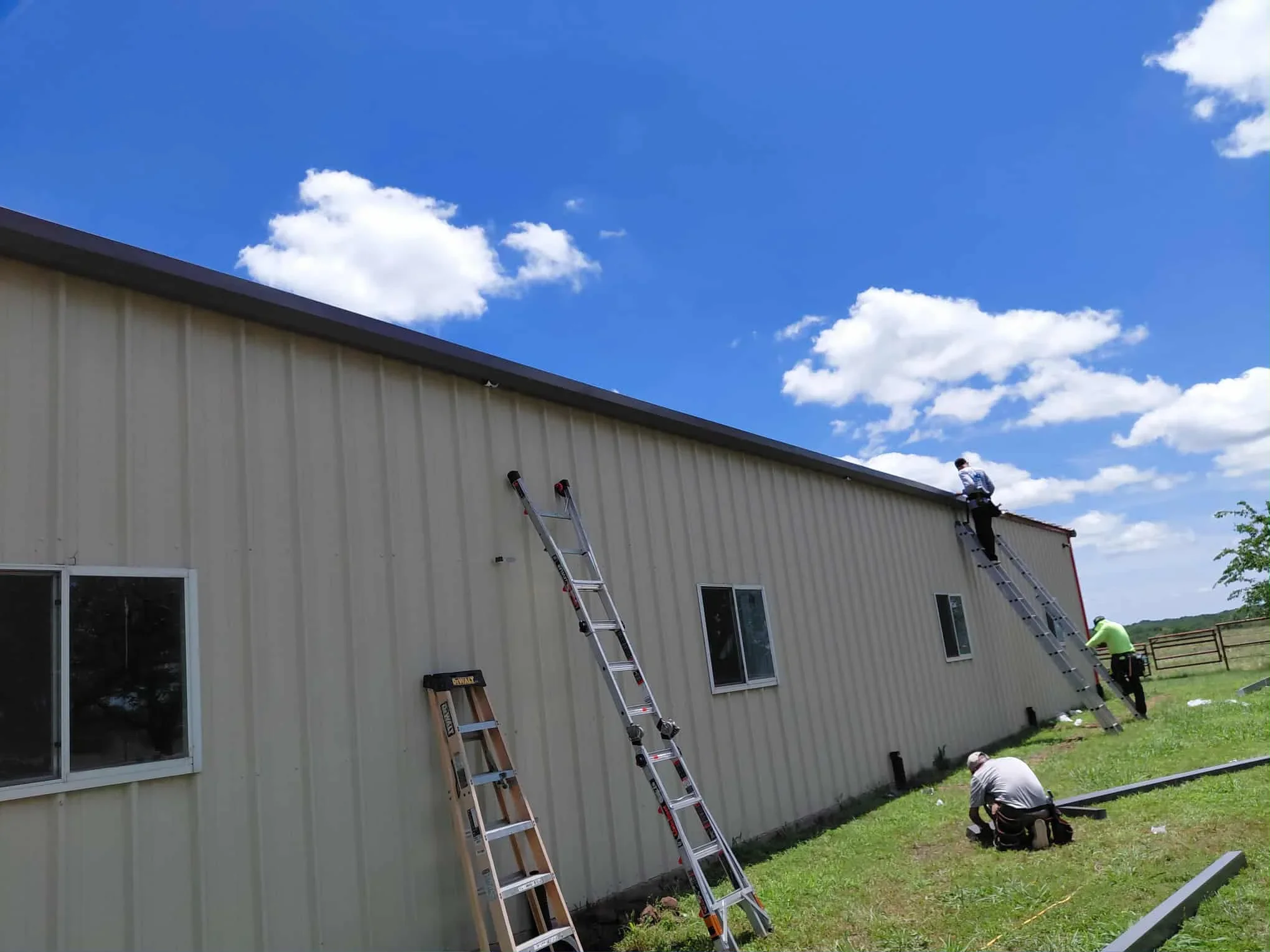 Metal building roof installation with corrugated panels and workers on ladders