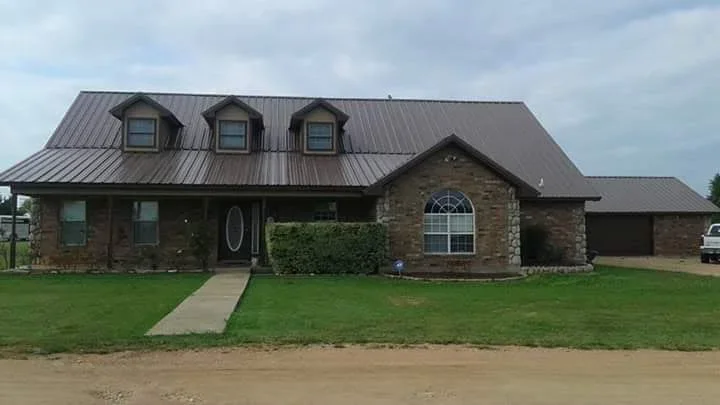 Standing seam metal roof installation on brick home with three dormers and attached garage