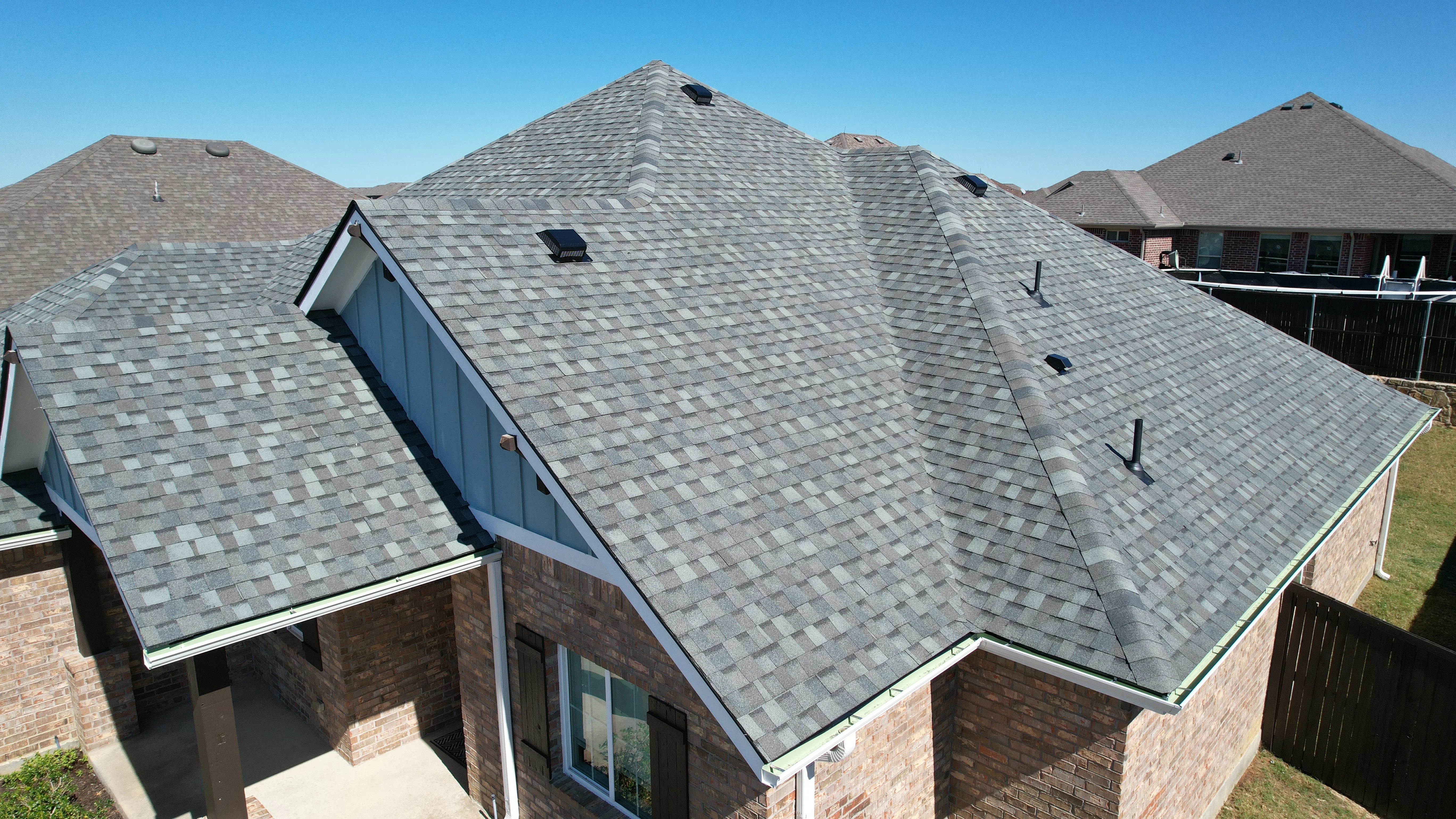 Gray architectural shingle roof with multiple peaks, skylights, and white gutter system on brick home