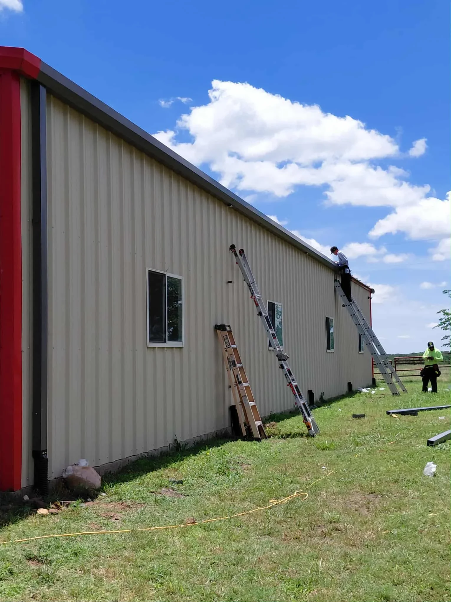 Crew installing corrugated metal roofing on agricultural metal building with ladders and safety equipment