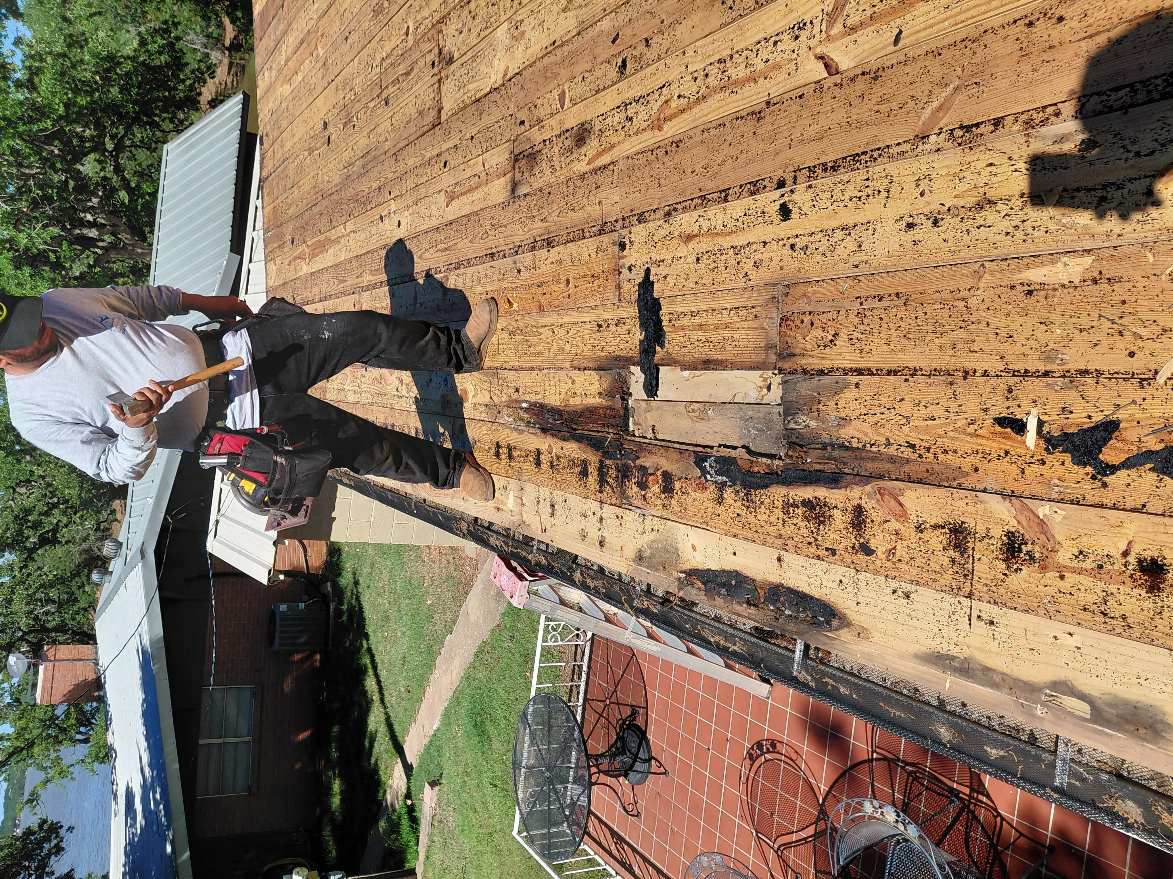 Worker inspecting damaged log roof beams with visible rot and deterioration on residential structure