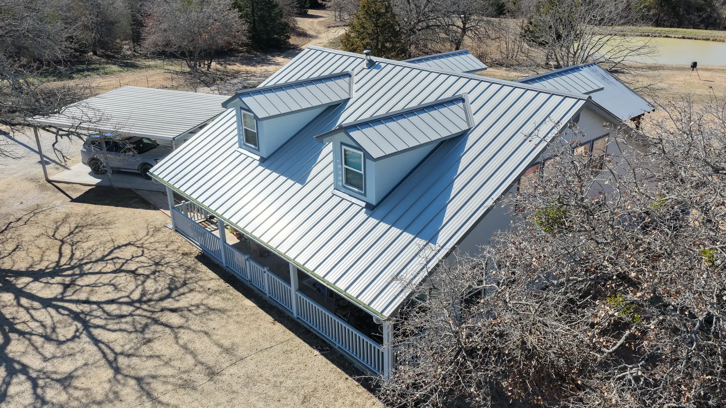 Standing seam metal roof with two dormers and white porch railings on residential home