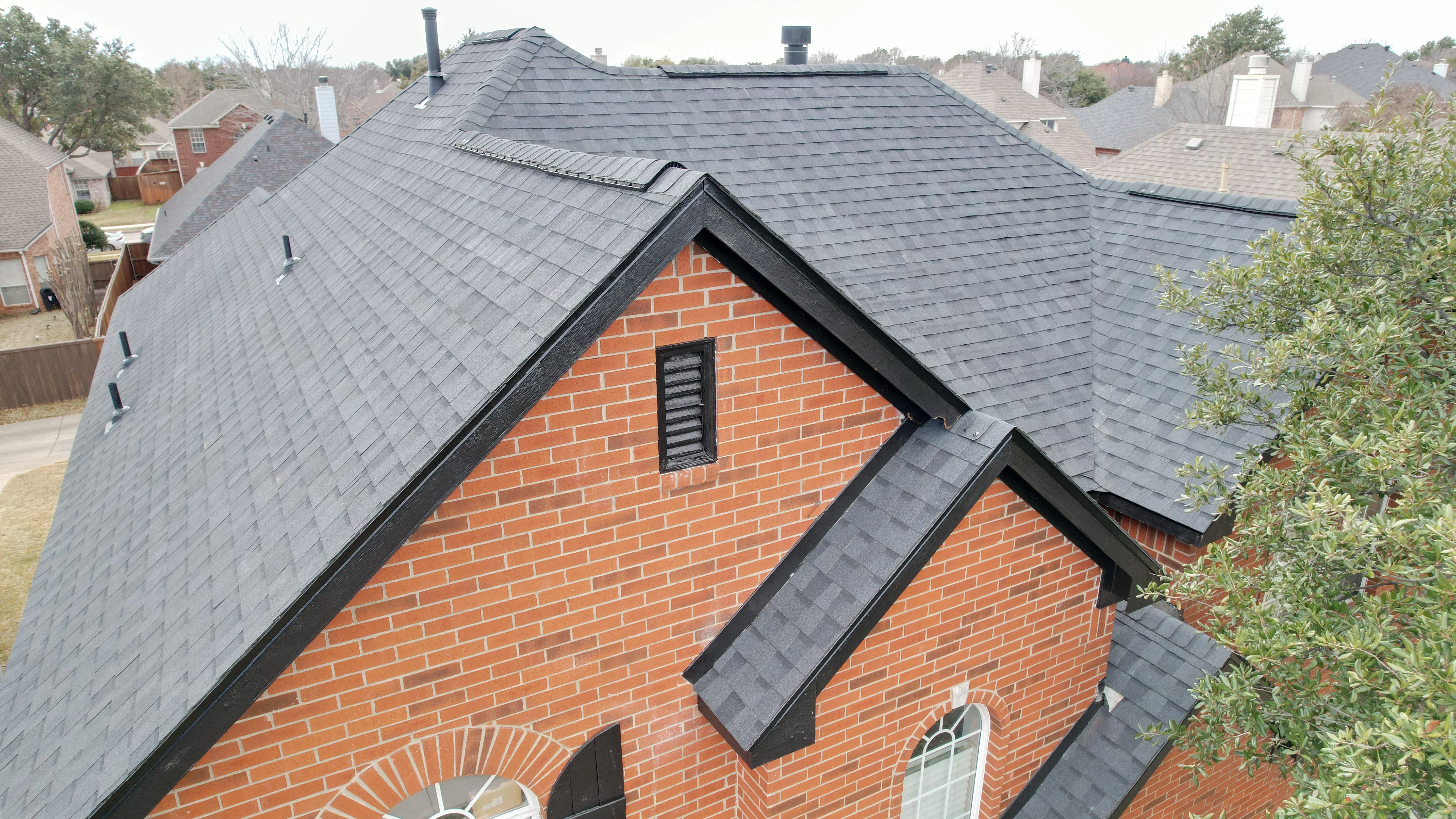 Gray architectural shingles on brick home with gables, dormers, and black trim flashing