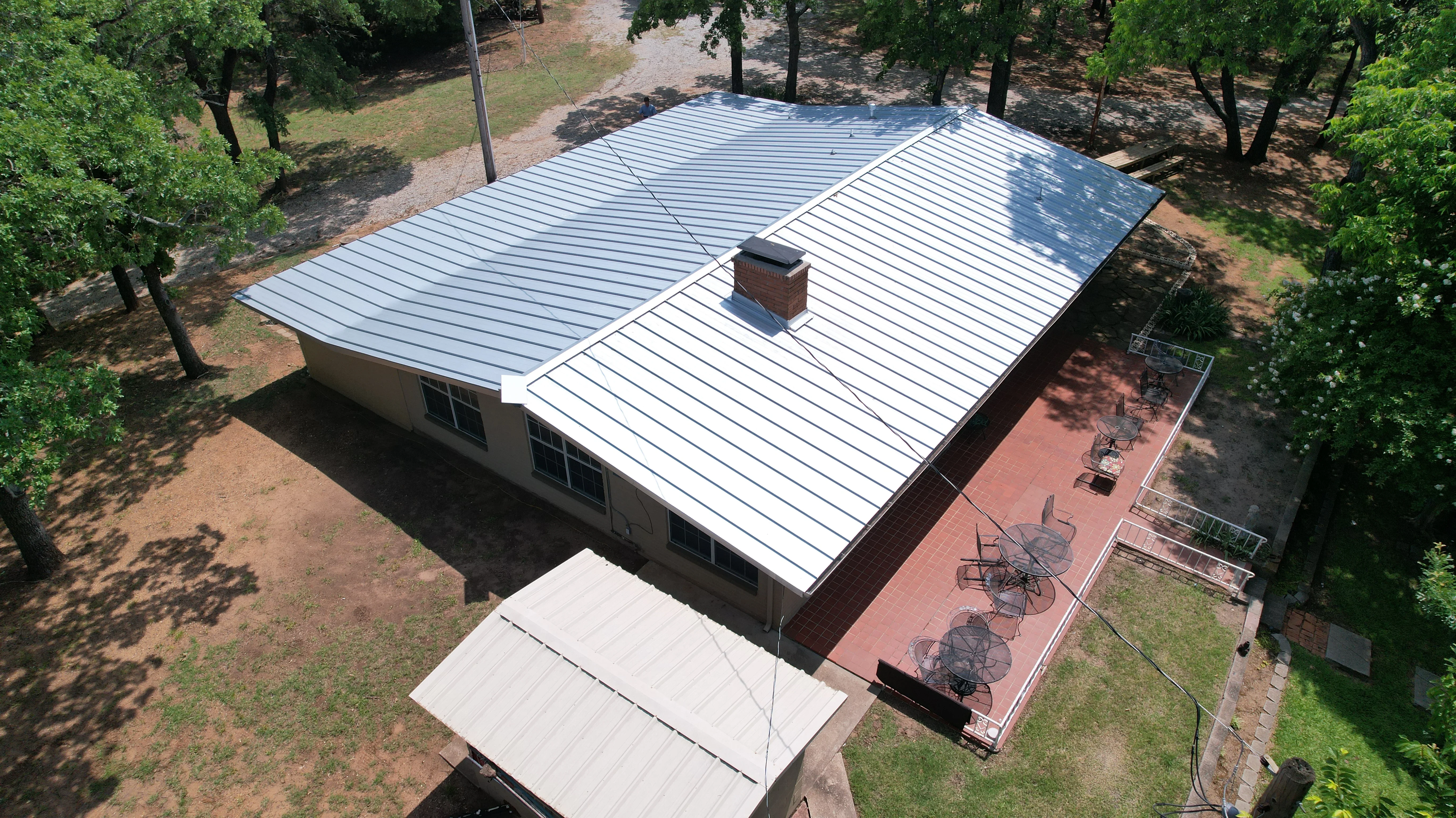 Standing seam metal roof with light gray panels and brick chimney on residential home