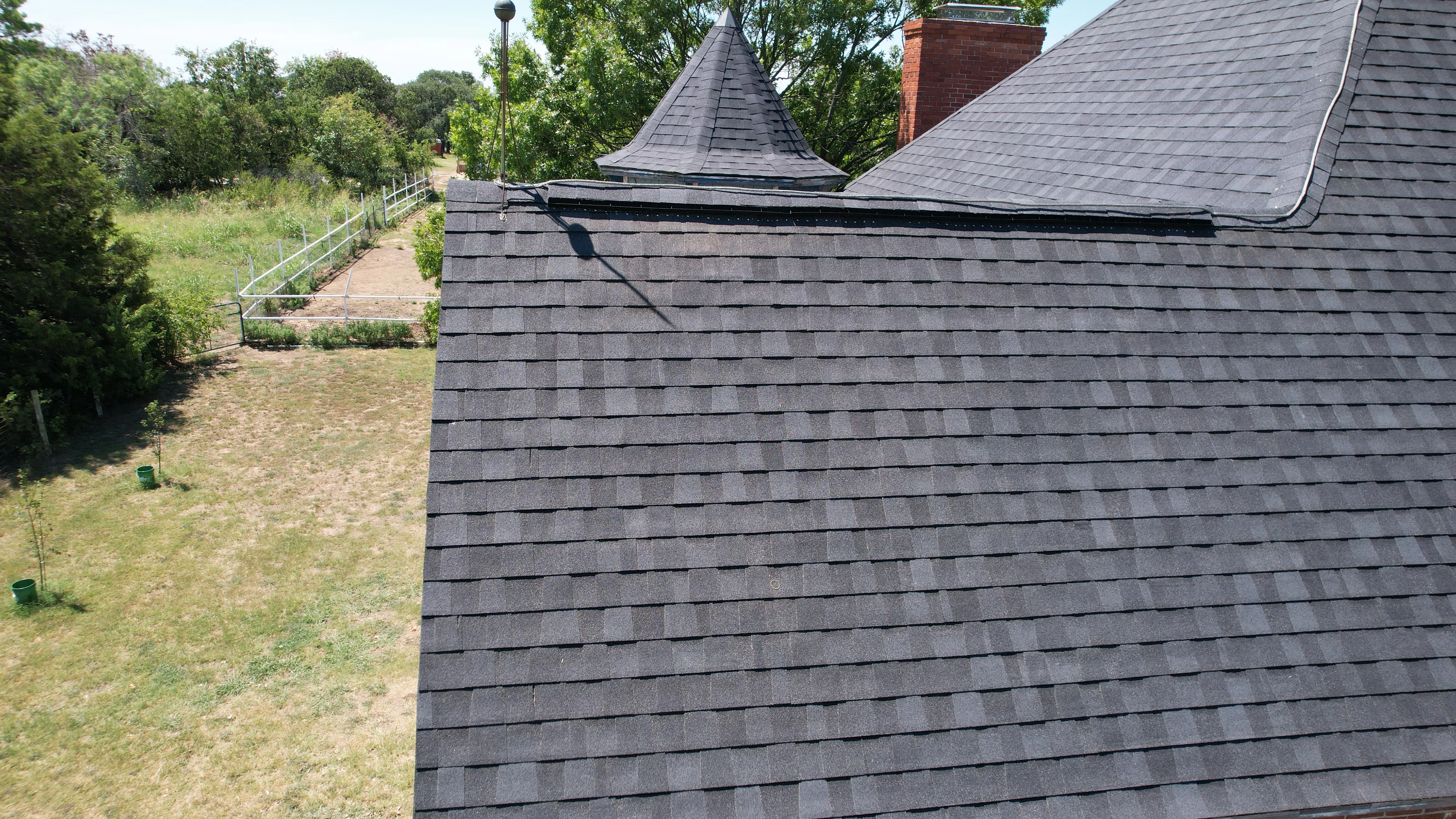 Charcoal gray architectural shingles installed on multi-slope roof with chimney flashing and turret detail