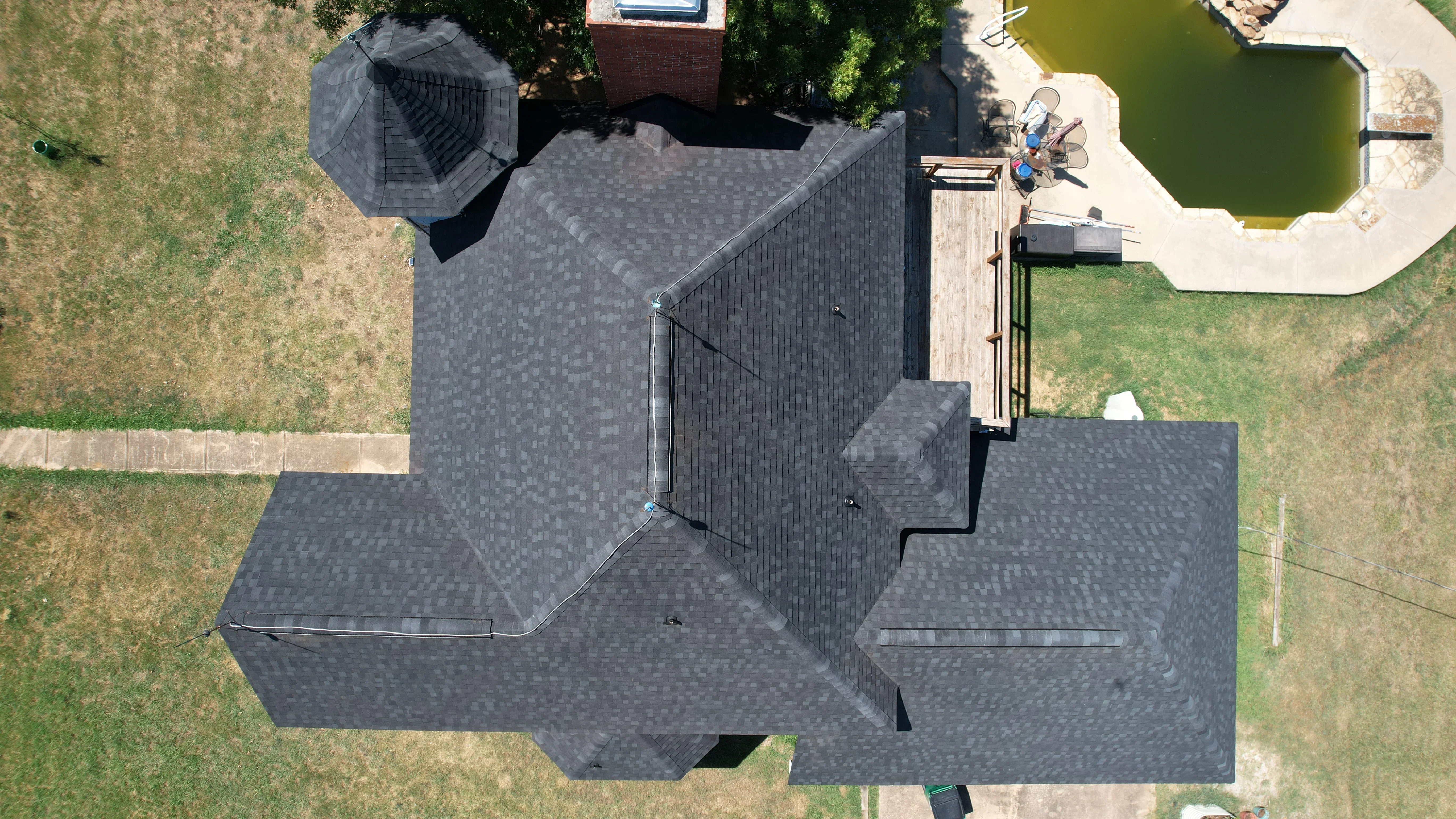 Aerial view of completed residential roof with charcoal gray architectural shingles and metal flashing