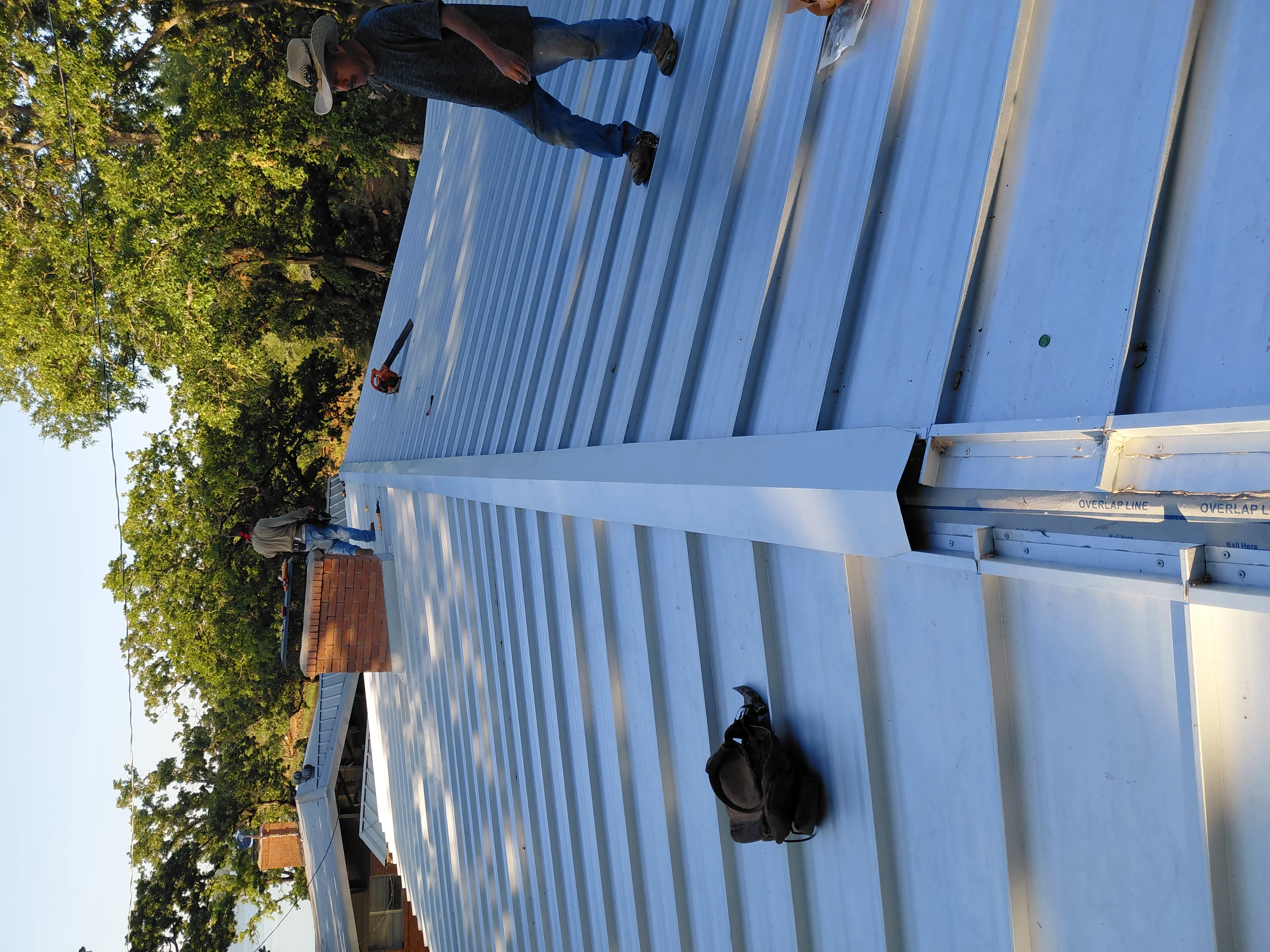 Standing seam metal roof installation with white corrugated panels and overlap sealing