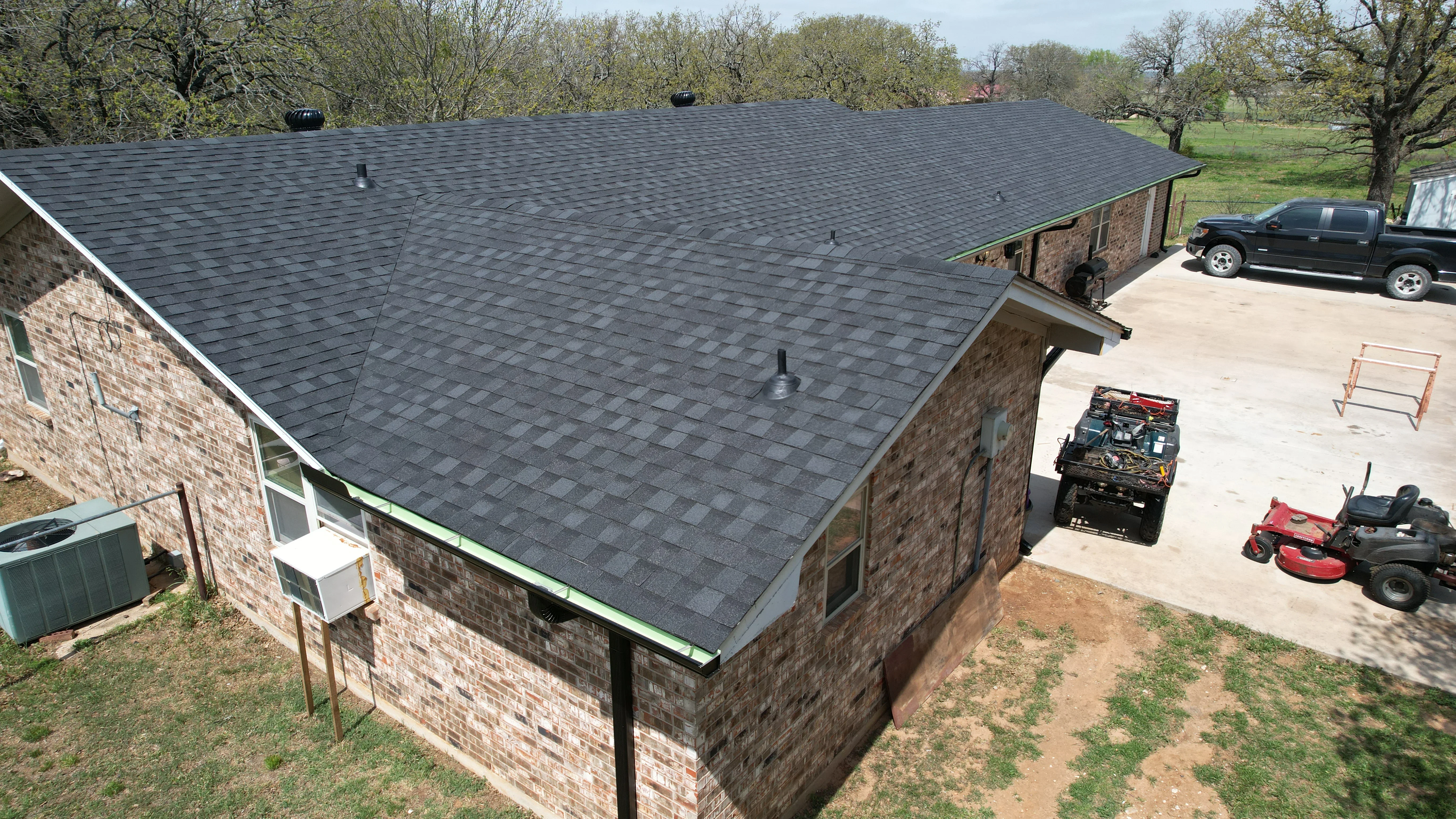 Charcoal gray asphalt shingle roof on brick home with ventilation and trim work