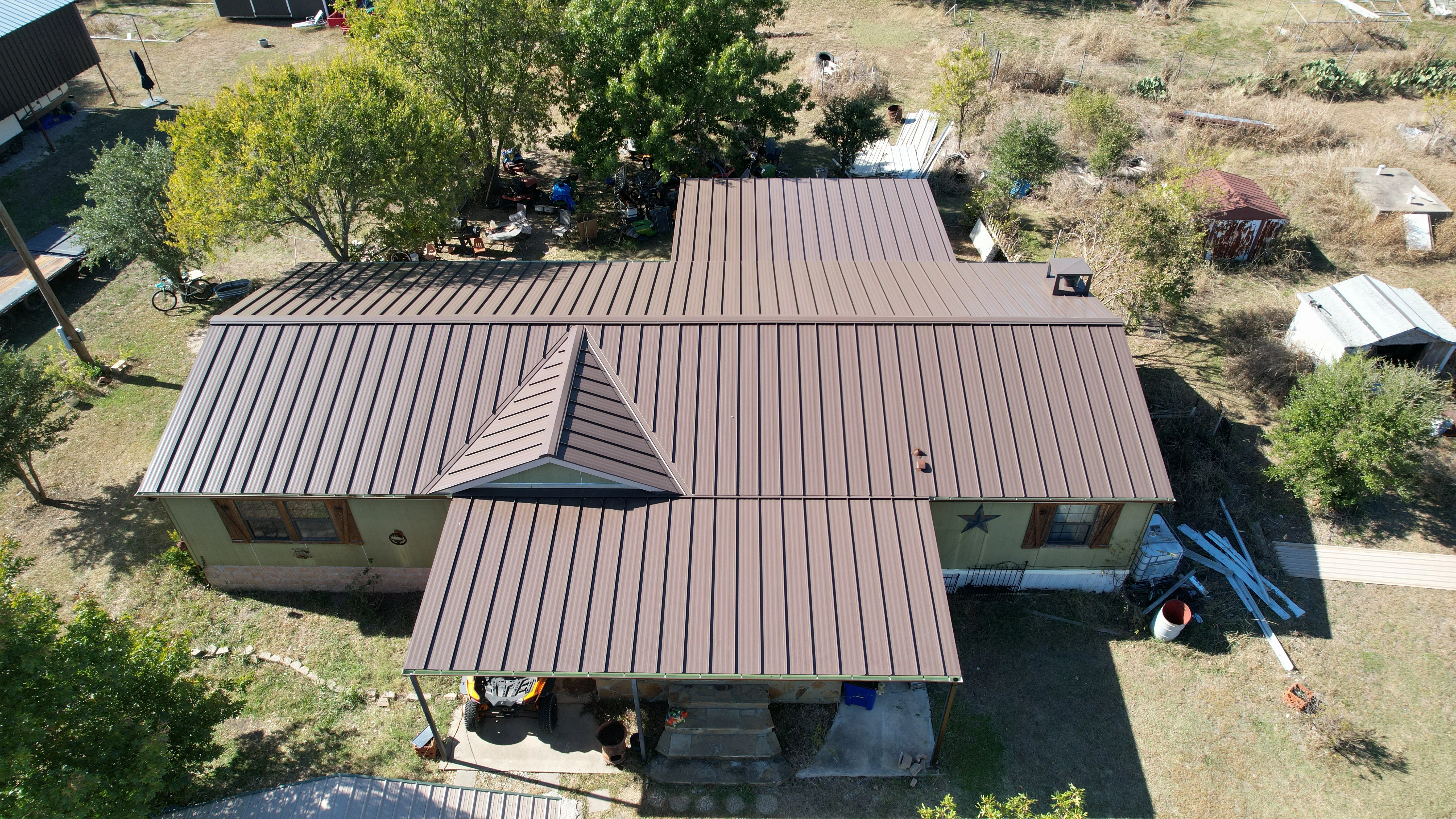 Aerial view of standing seam metal roof installation with brown panels and central gable on residential structure