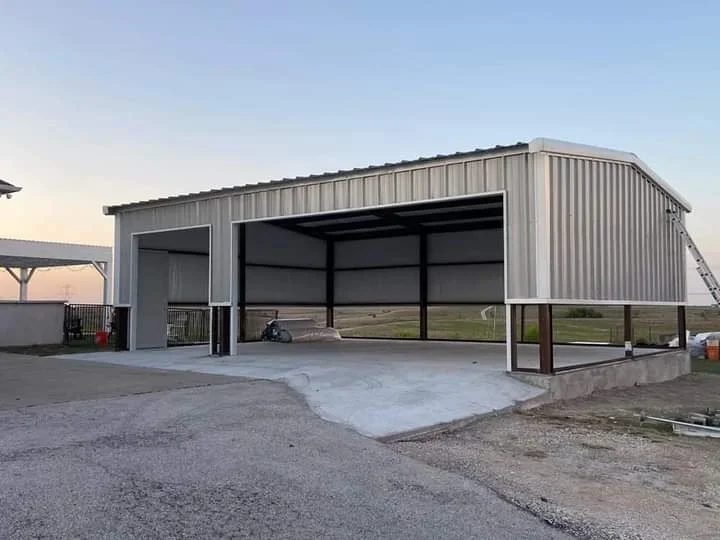 Metal pole barn with corrugated steel siding, open lean-to bay, and concrete pad foundation
