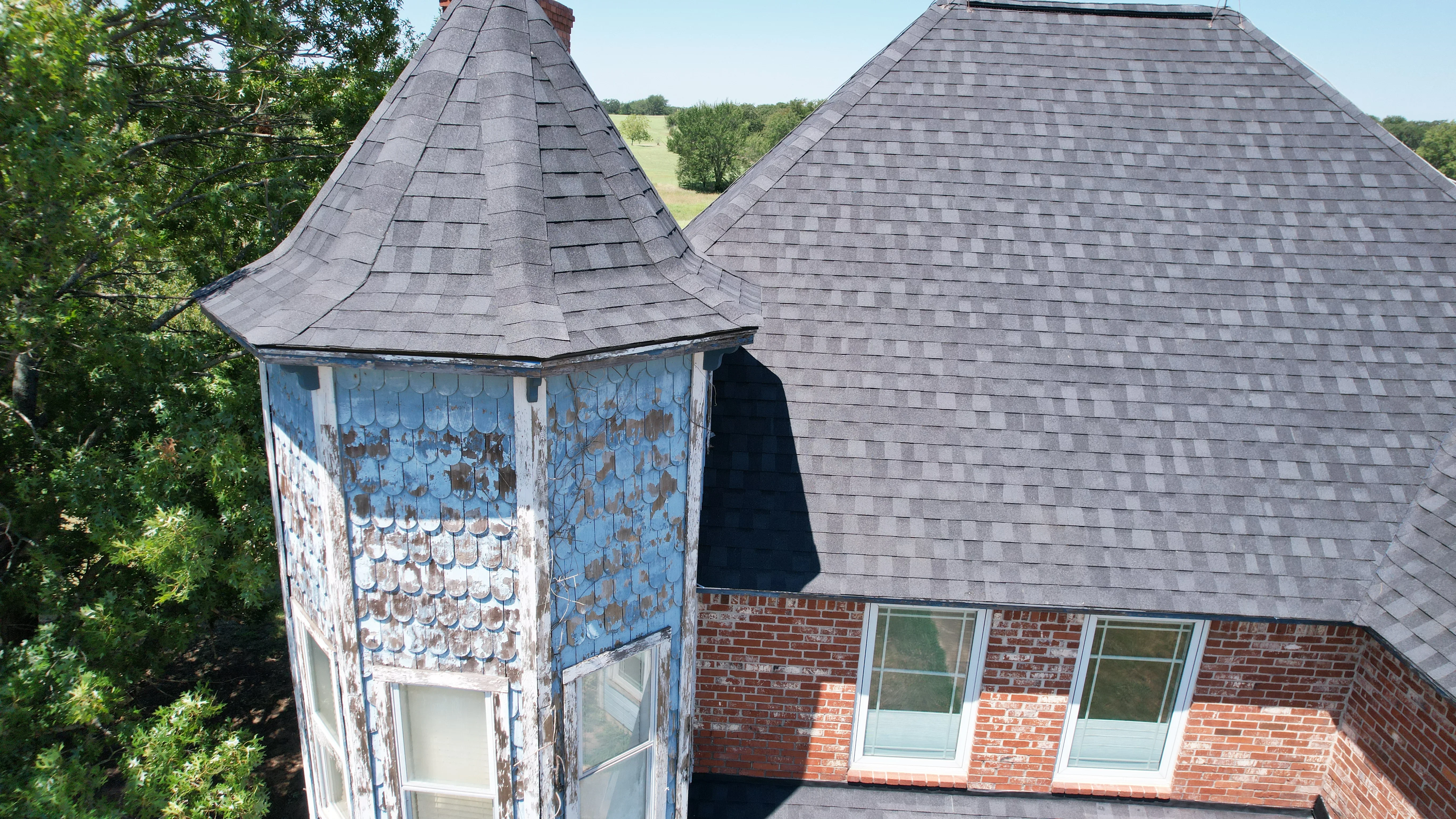 Charcoal gray architectural shingle roof installation on brick home with turret and gable sections