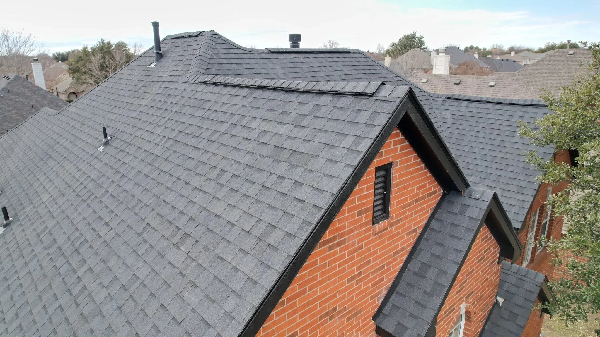 Charcoal gray standing seam metal roof on brick home with gable vents and multiple roof planes