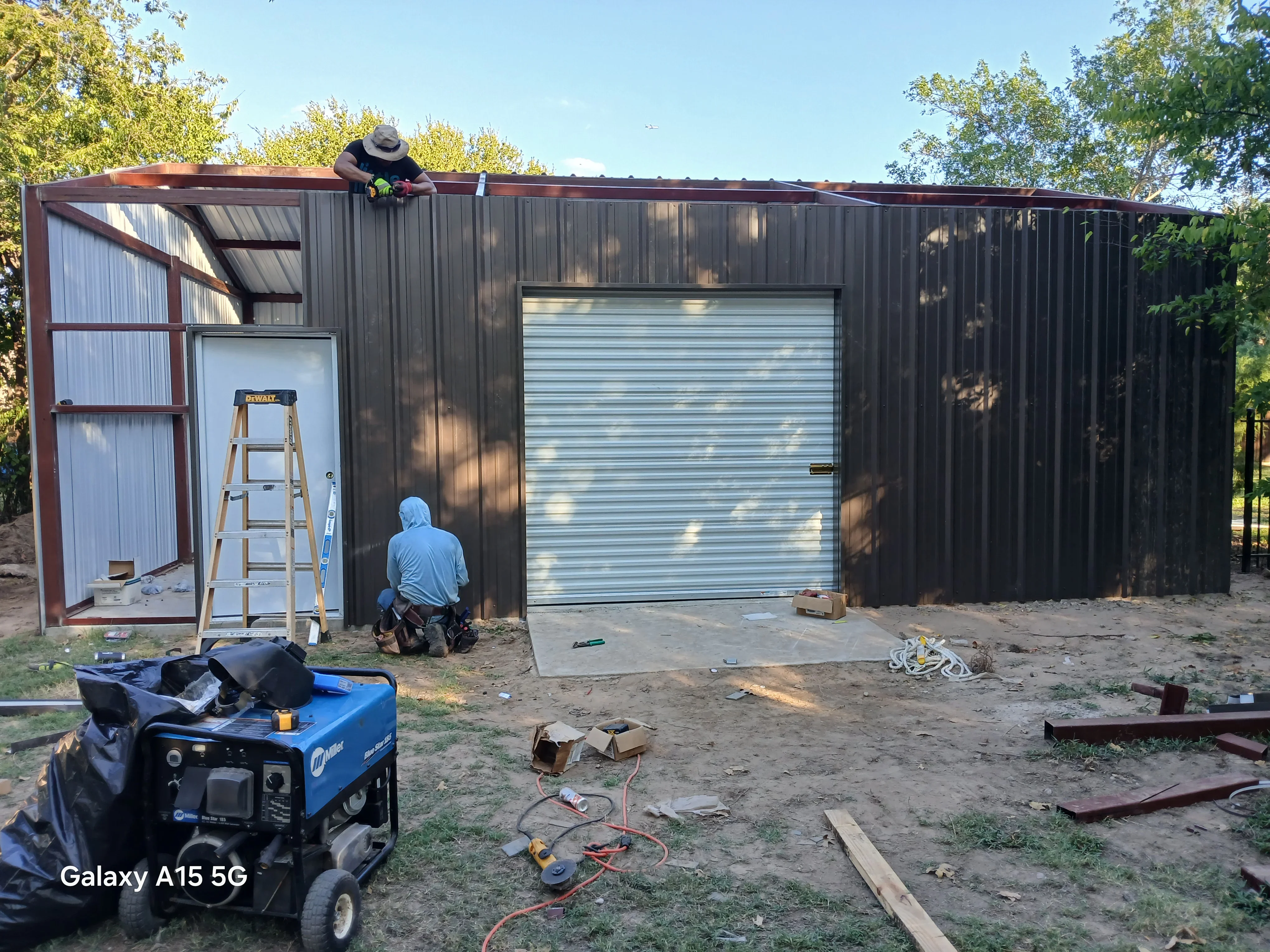 Metal building with corrugated steel siding, standing seam roof, and garage door during construction