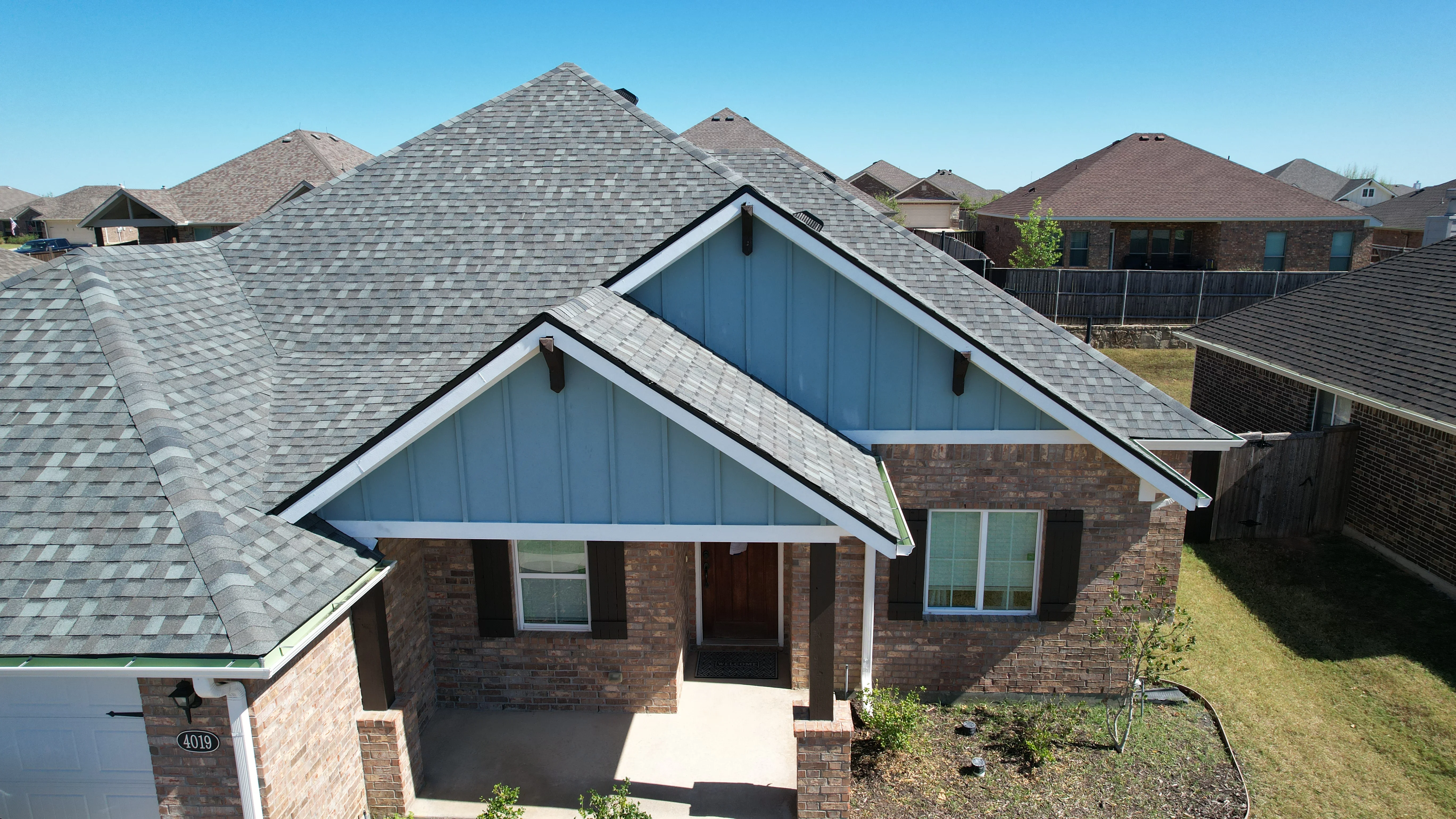 Gray architectural shingle roof with multiple peaks and gable vents on brick home