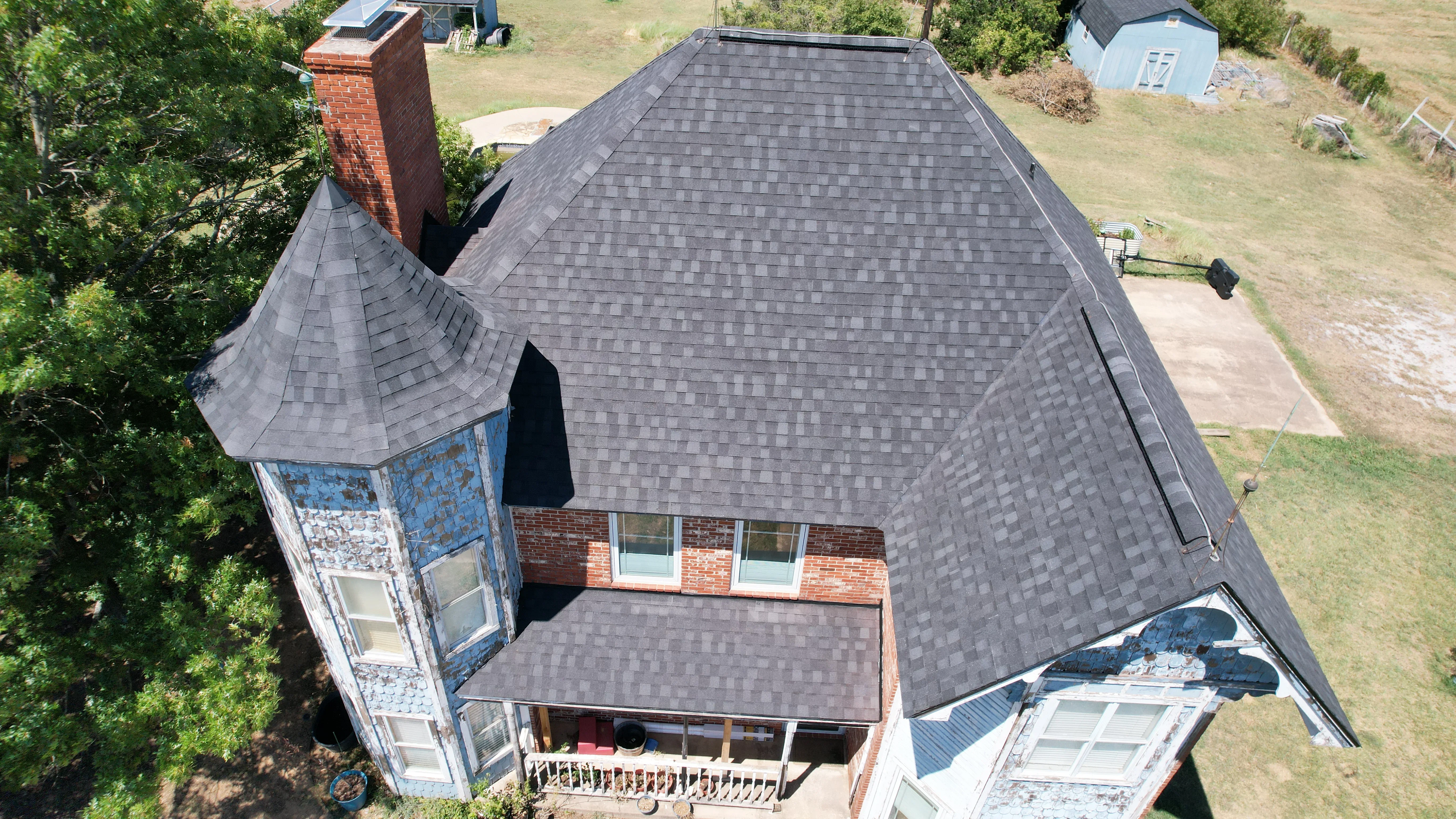Gray asphalt shingle roof installation on brick home with turret and chimney