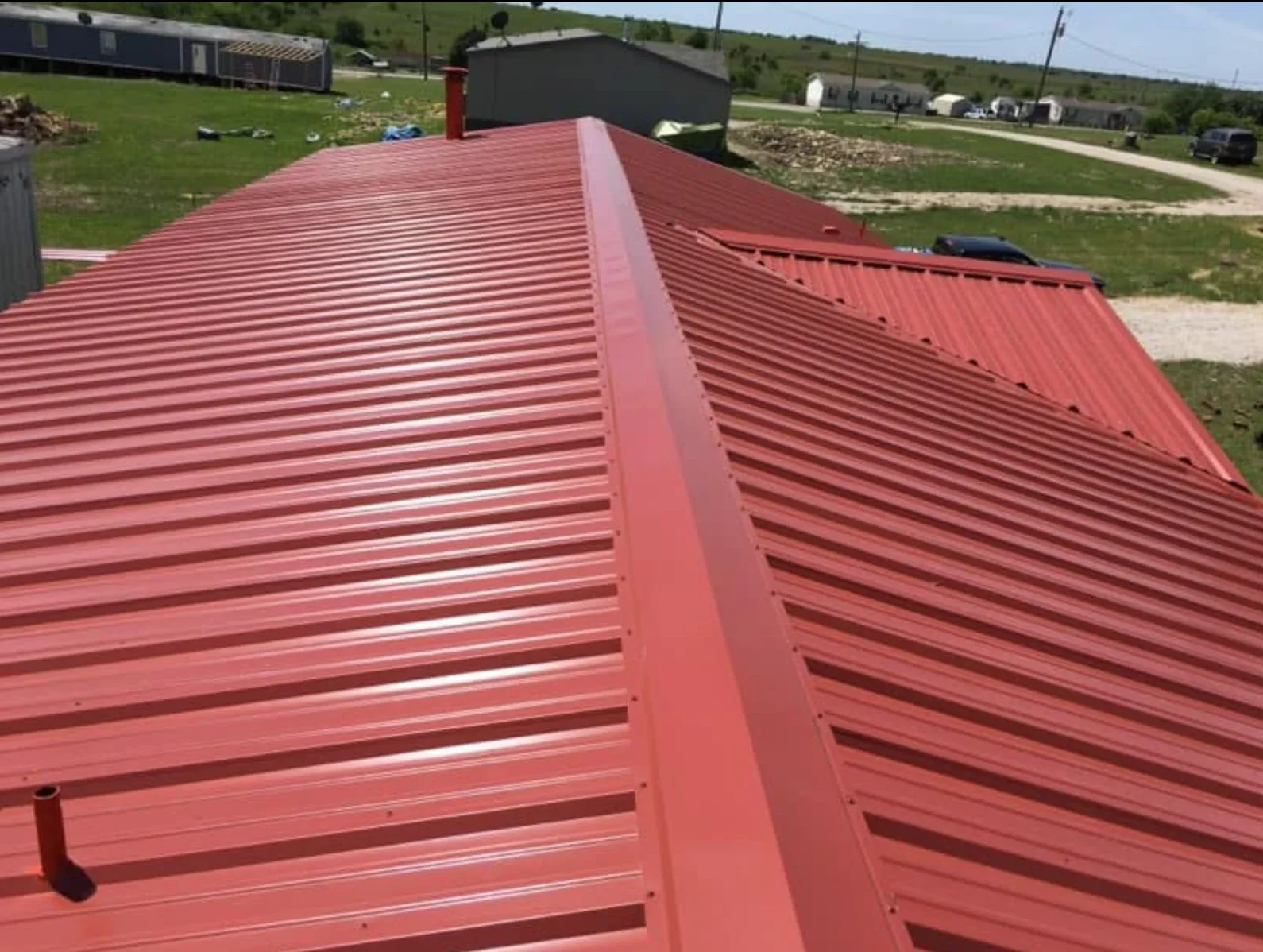Red corrugated metal roof panels with ridge cap and fasteners installed on pitched structure
