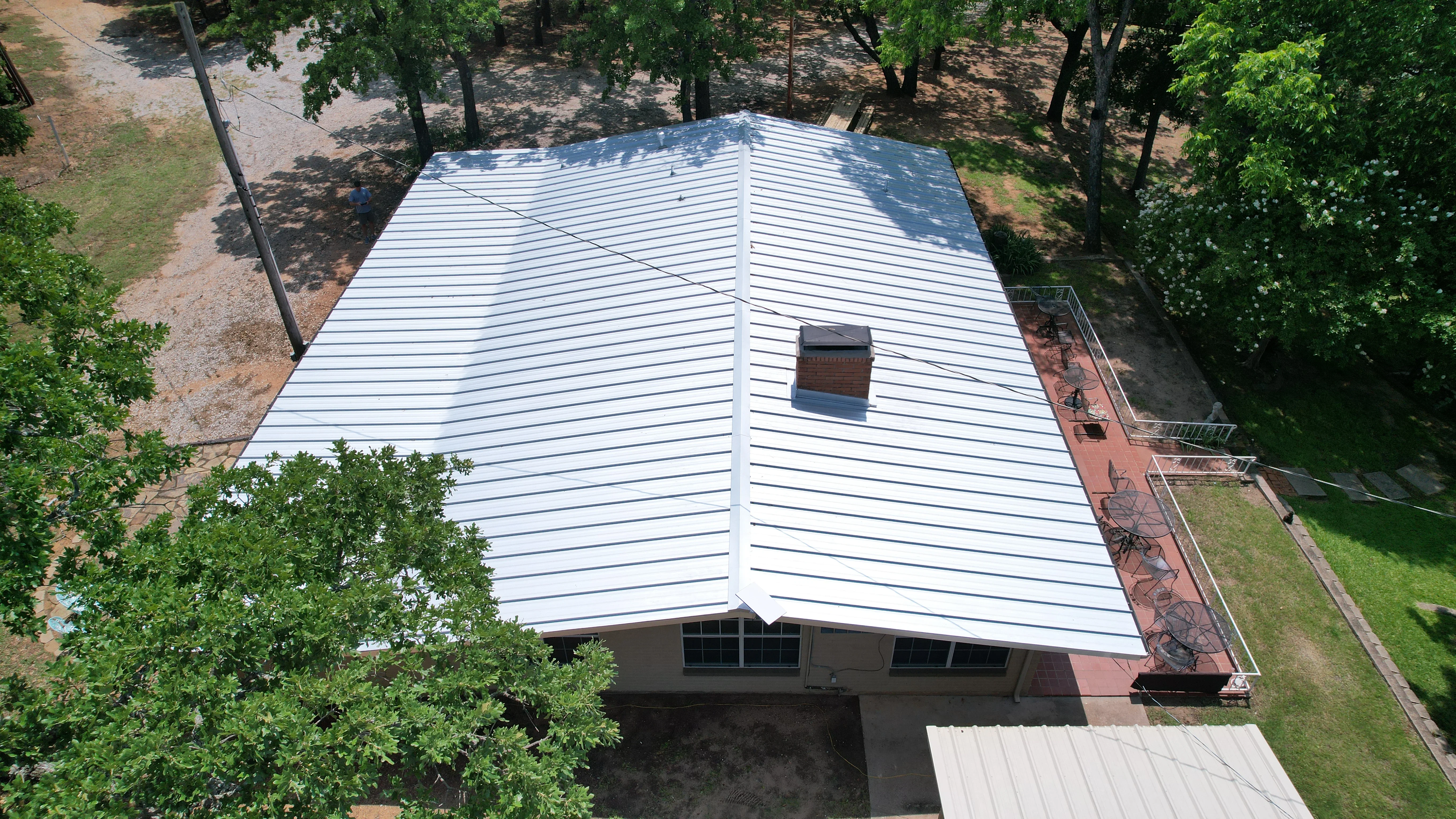 White standing seam metal roof with gabled design and brick chimney on residential structure
