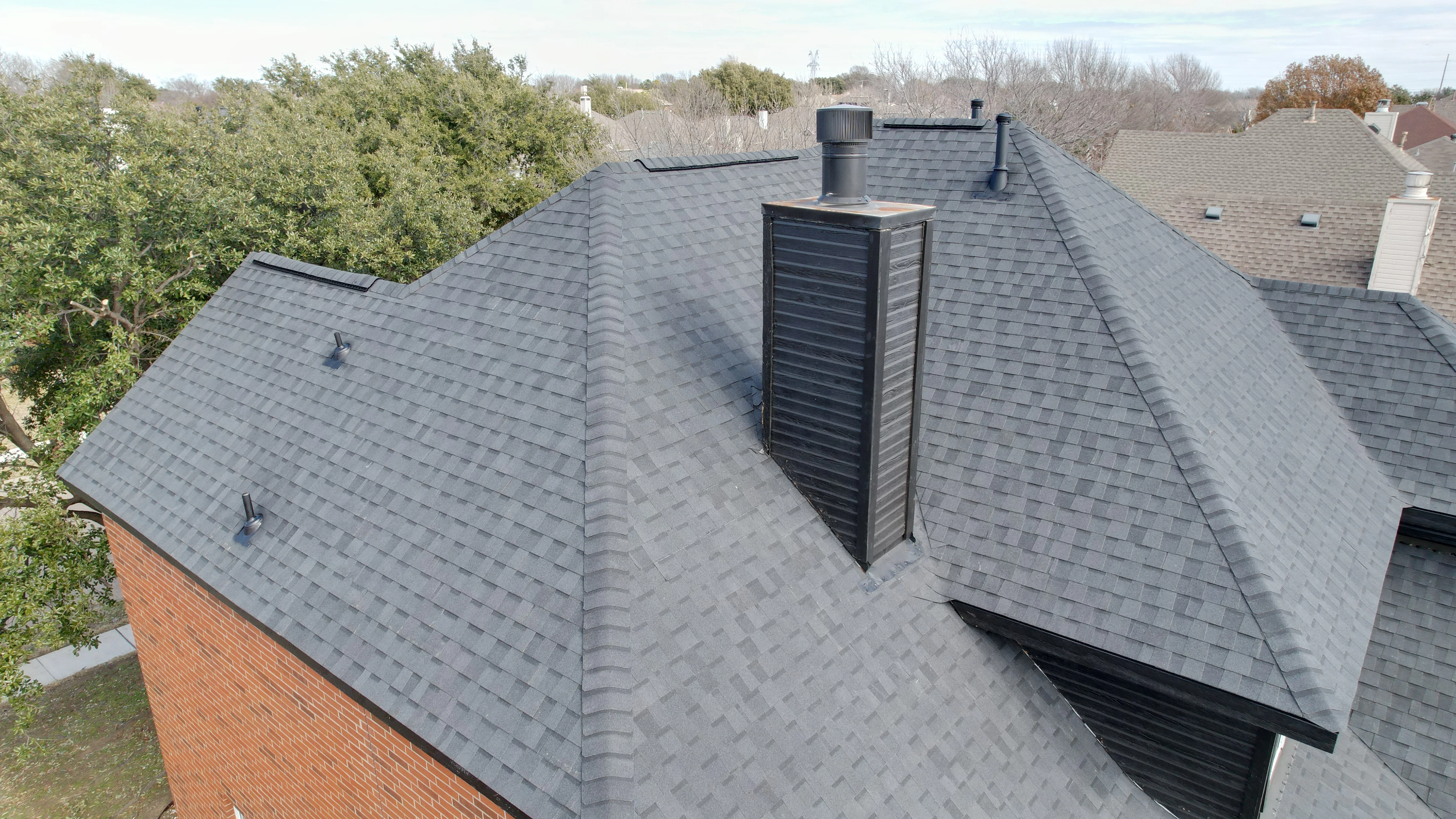 Charcoal gray asphalt shingle roof with multiple planes, valleys, and roof vents on brick home