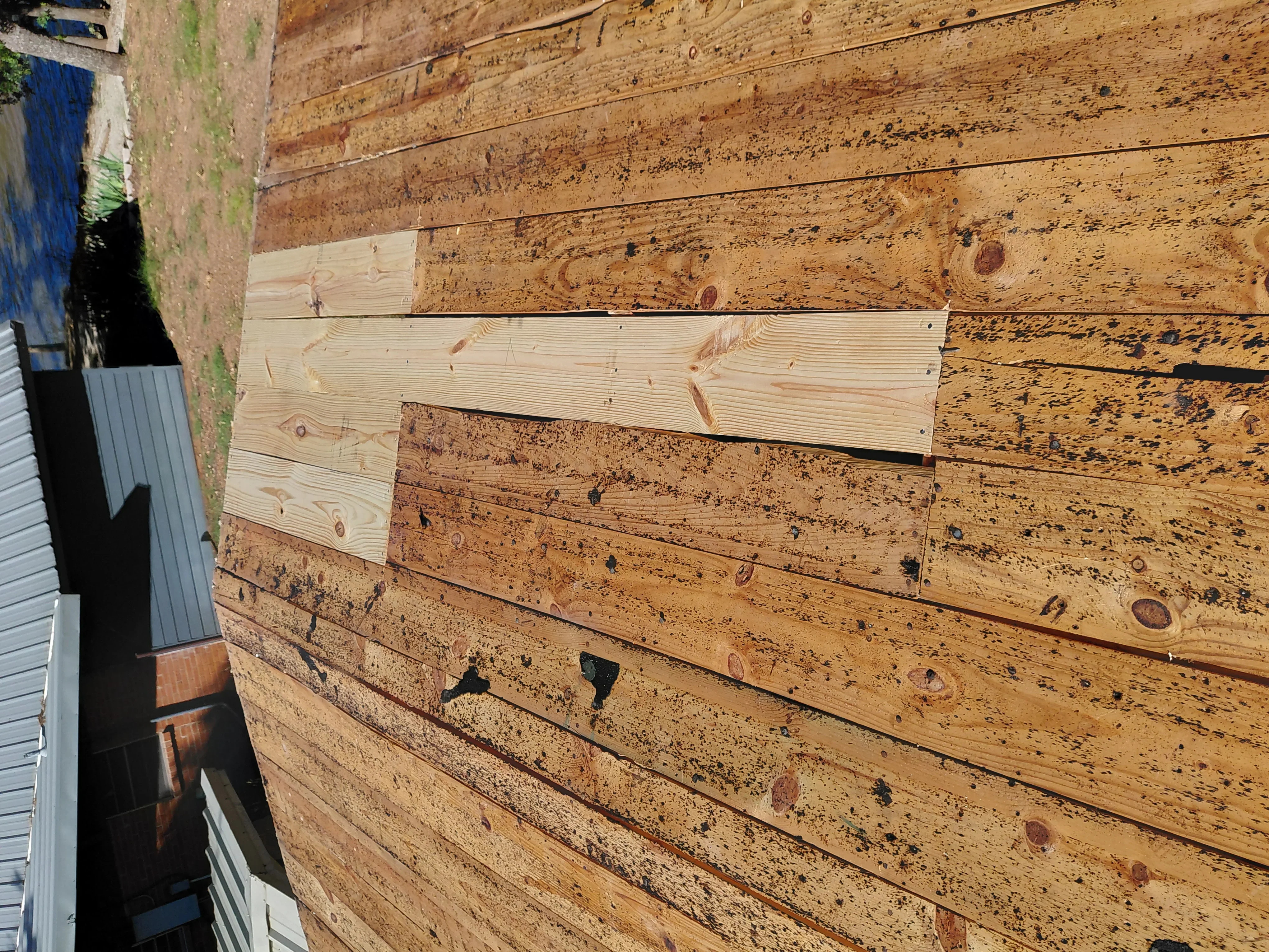 Wood siding repair with new pressure-treated boards replacing weathered and damaged horizontal planks