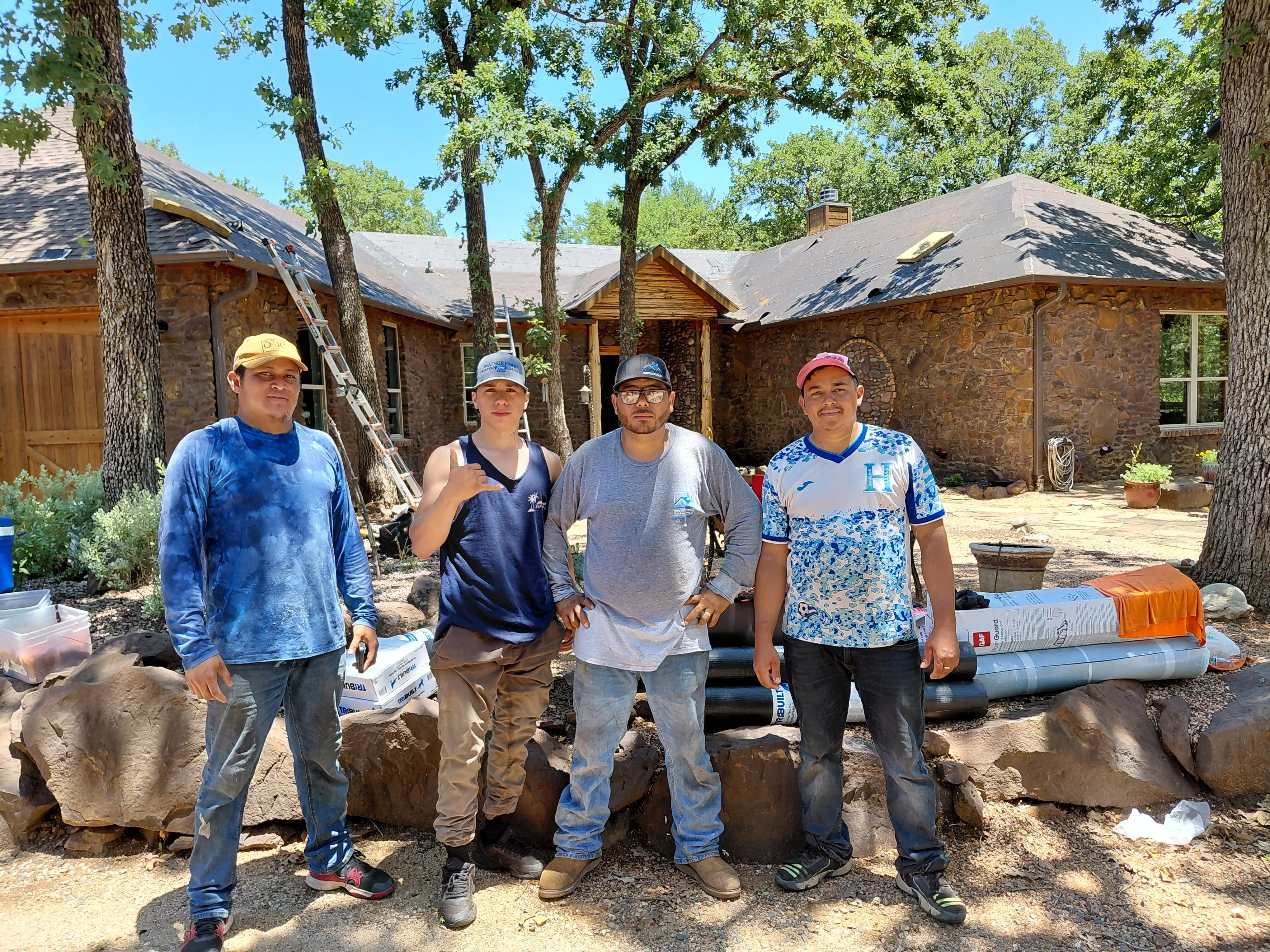 Metal roof installation on stone home with multiple pitched roof sections and work crew