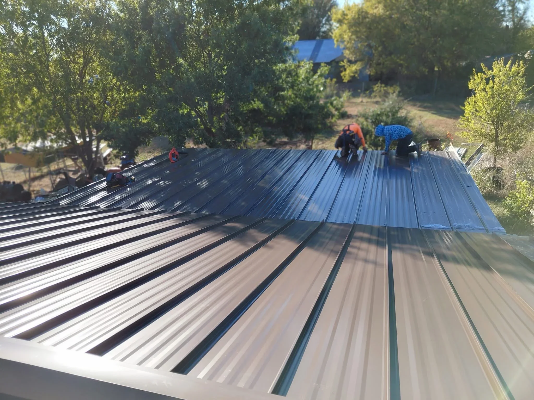 Standing seam metal roof installation with blue corrugated panels and workers fastening sheets