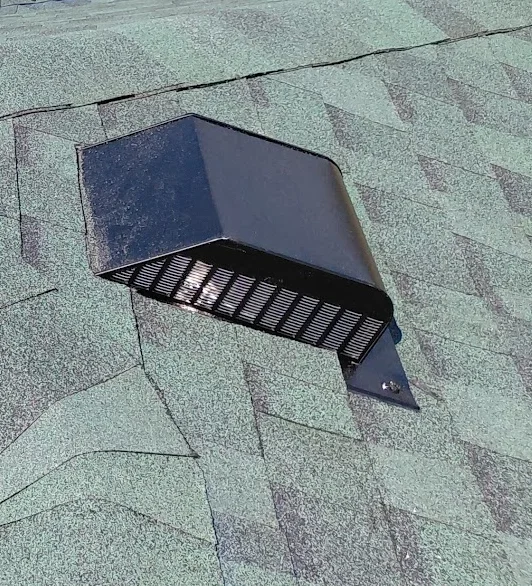 Black metal roof vent with louvers installed on asphalt shingle roof