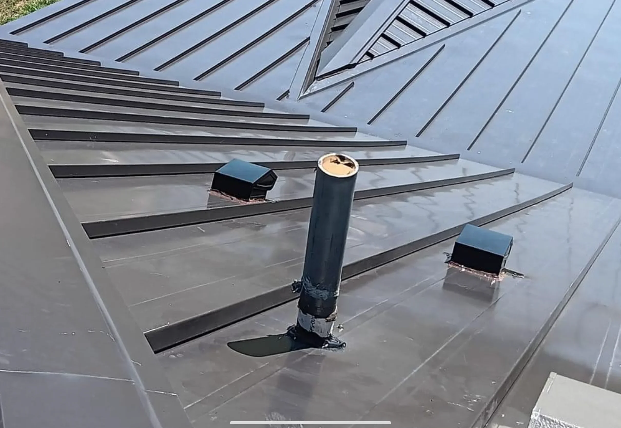 Standing seam metal roof with black ribs, flashed vents, and roof penetrations