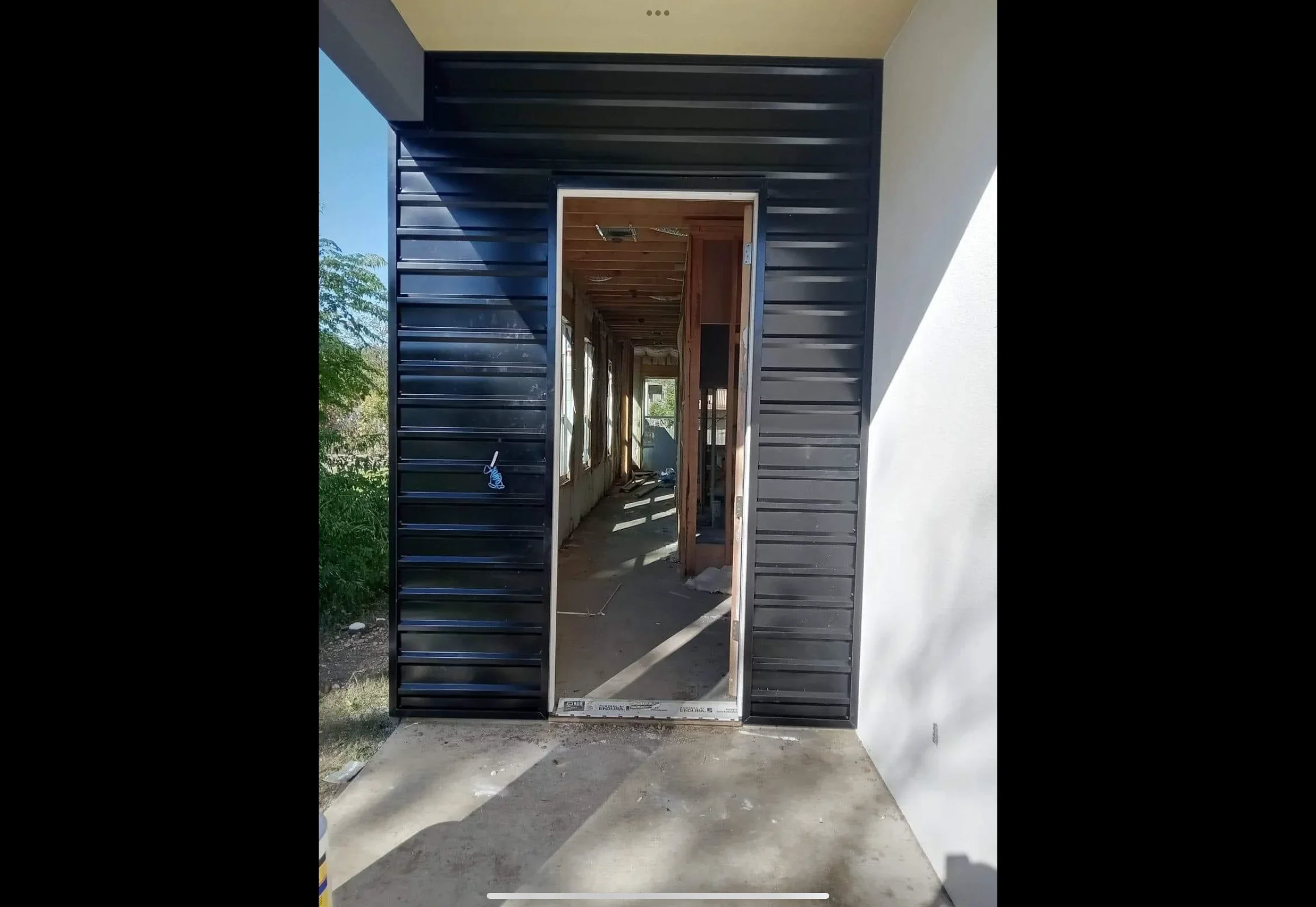 Charcoal corrugated metal siding with white-trimmed glass entry door and metal soffit