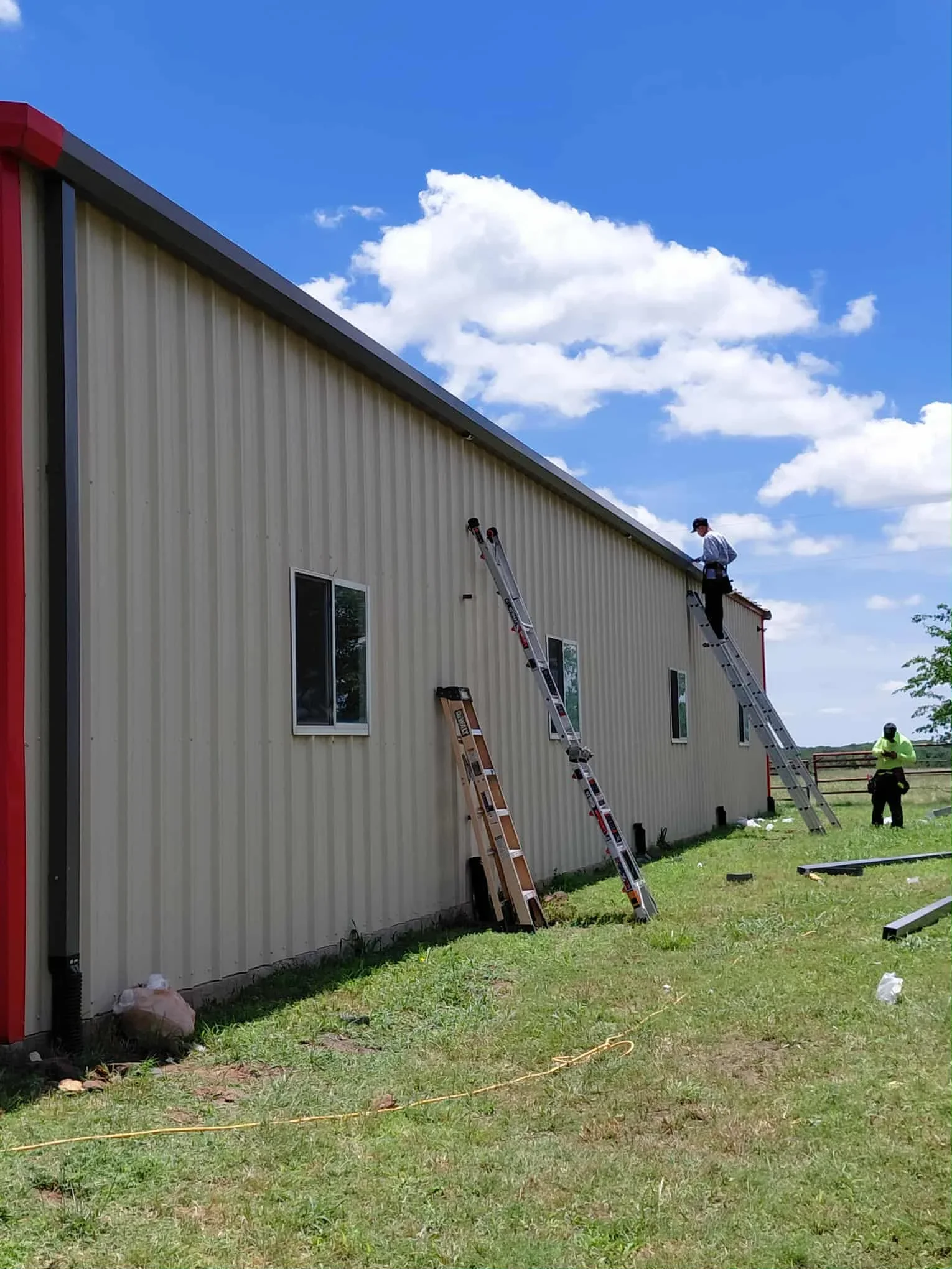 Metal roof installation on corrugated steel building with workers on ladders