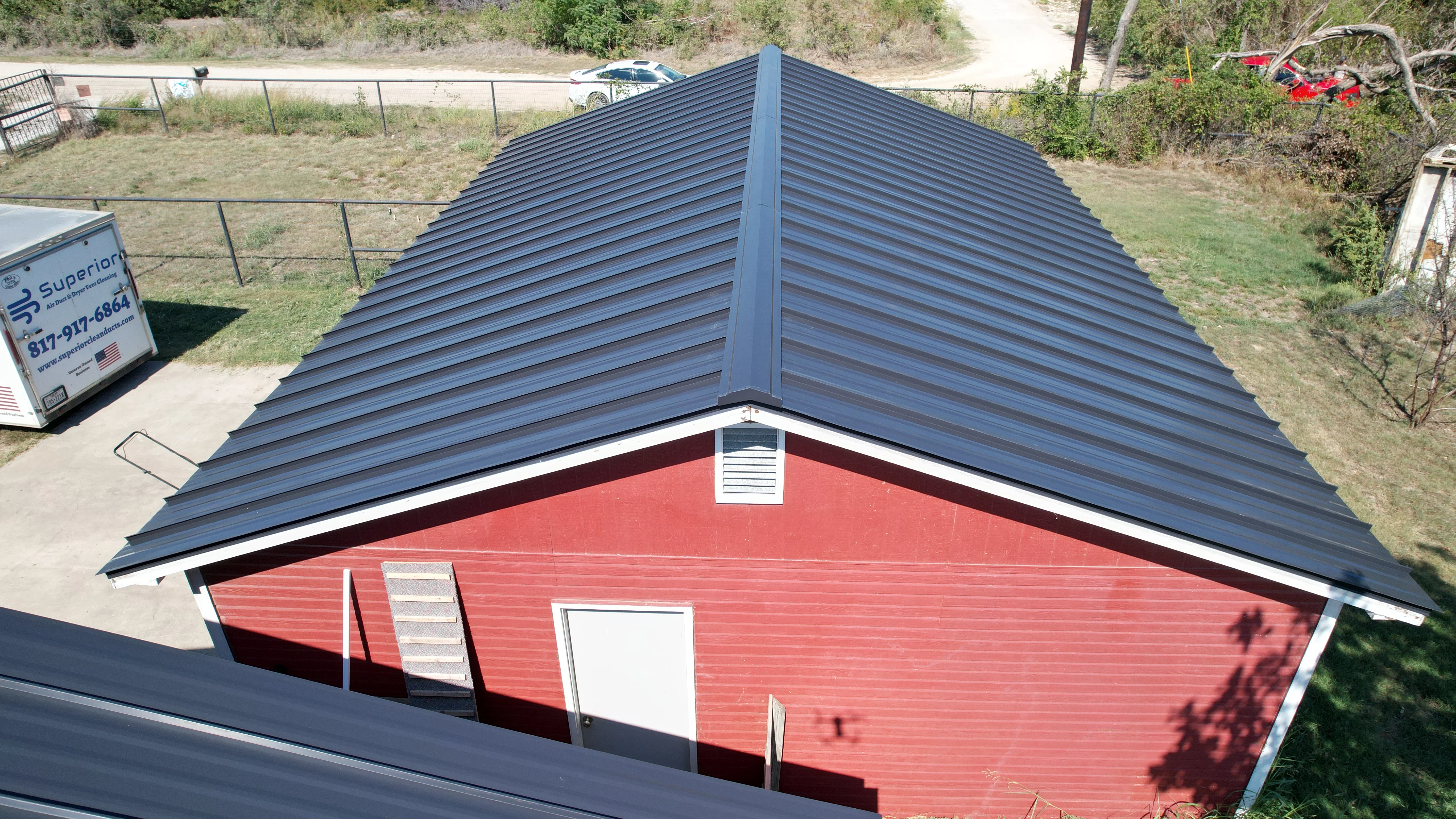 Dark blue standing seam metal roof on red metal building with ridge vent and white trim